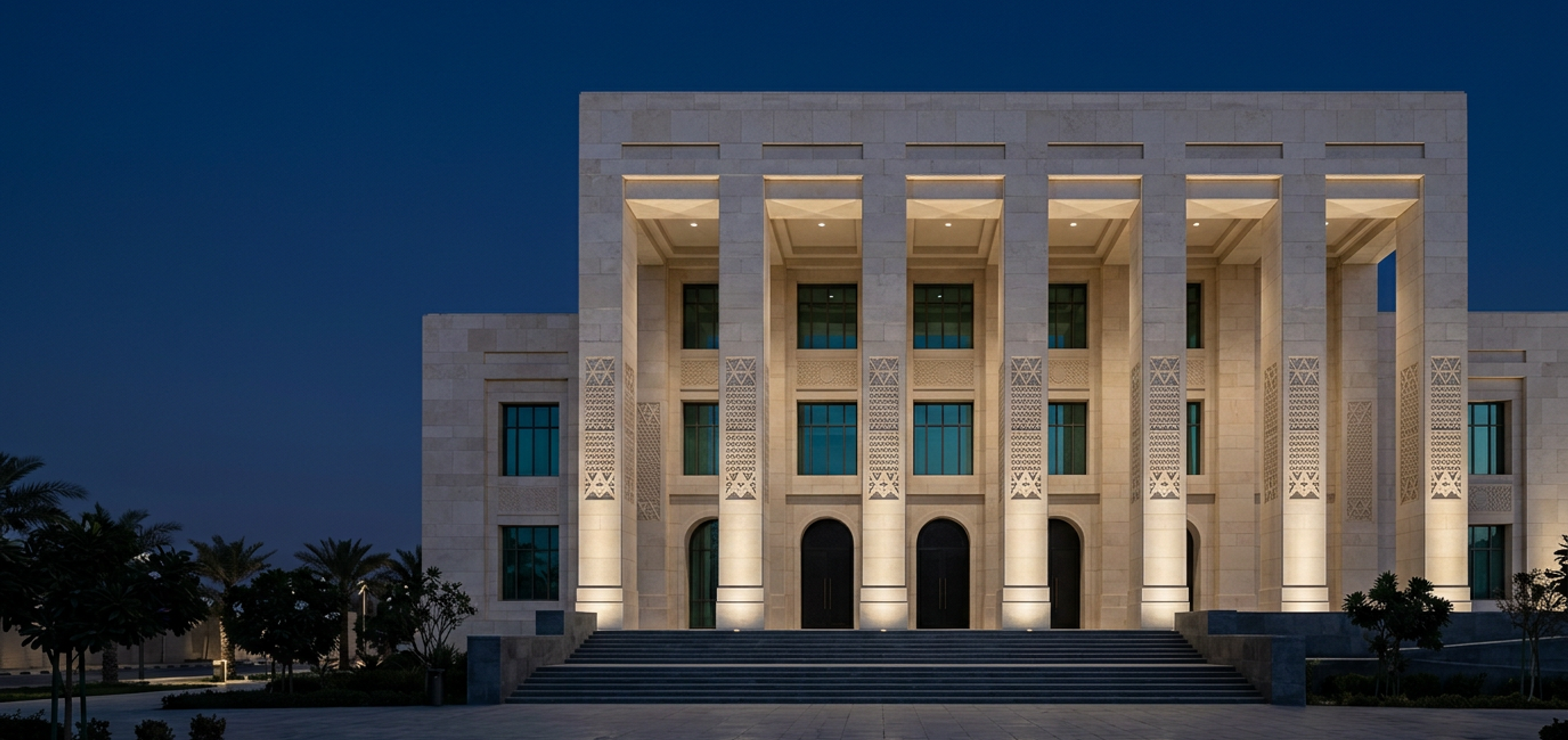The limestone colonnade of a modern Saudi government institution in Riyadh, softly uplit at blue hour.