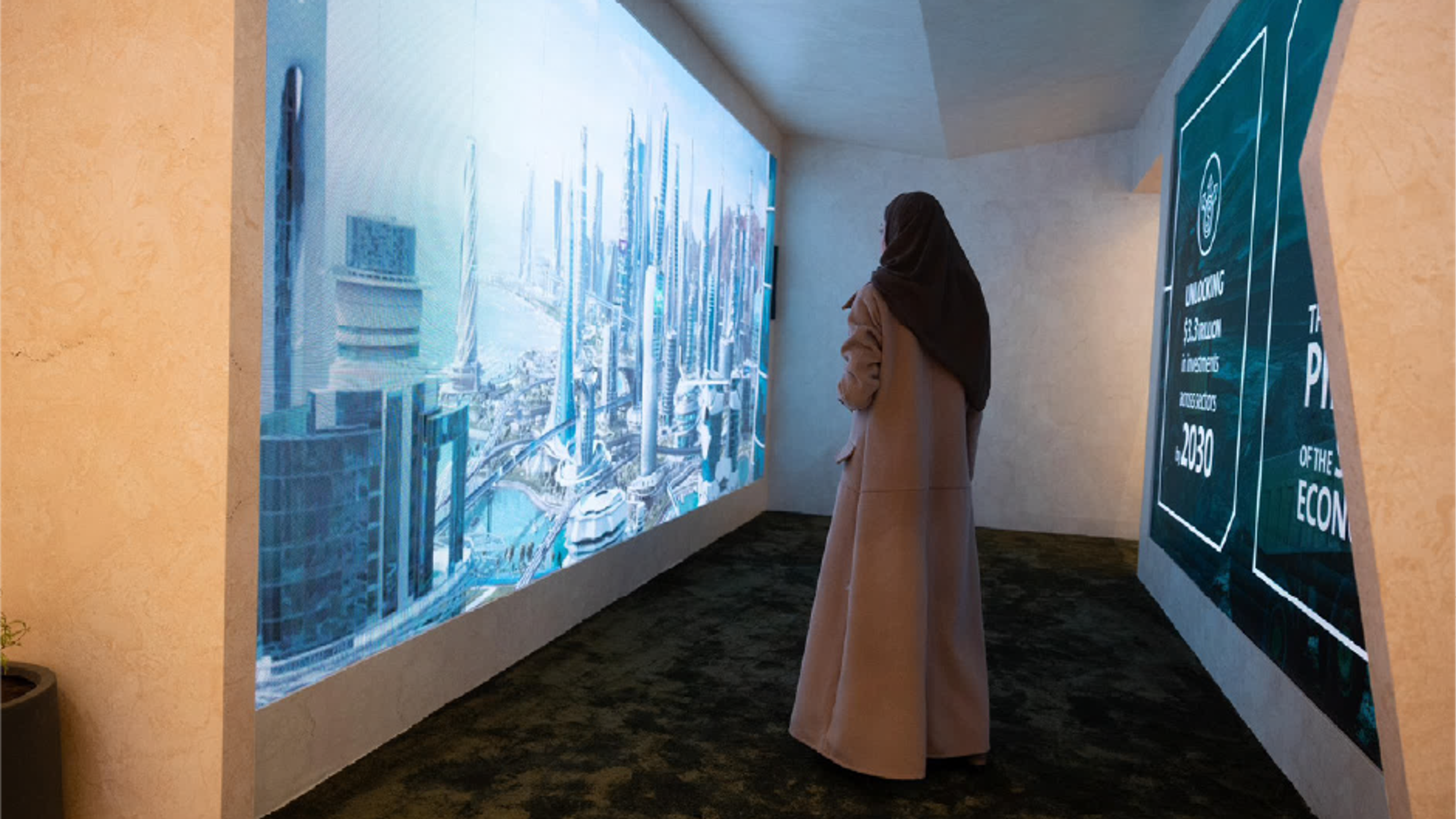 A woman stands in a darkened exhibition room, facing a wall-sized projection of a futuristic city skyline.