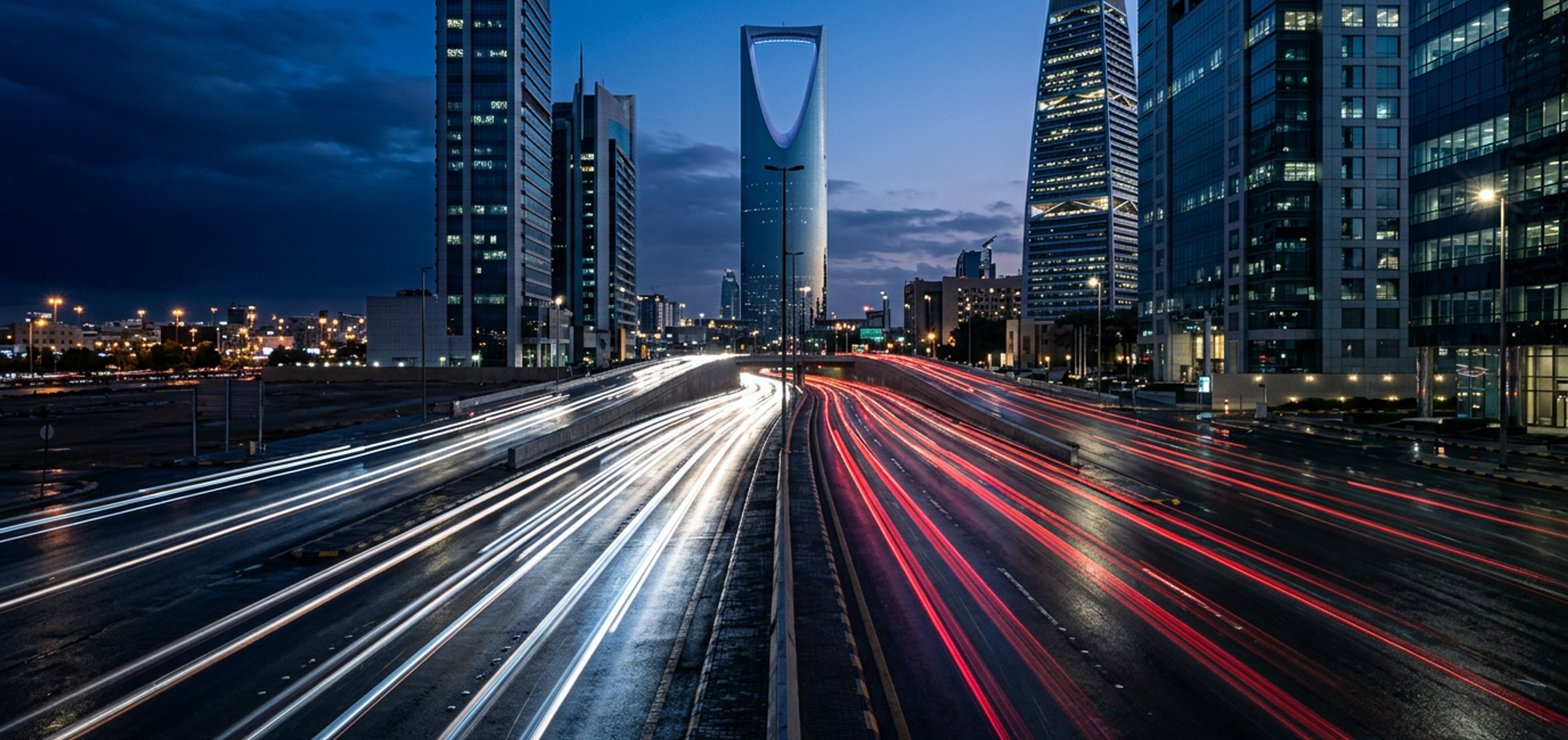 Light trails along King Fahd Road in Riyadh’s Olaya district at blue hour, the Kingdom Centre rising ahead.