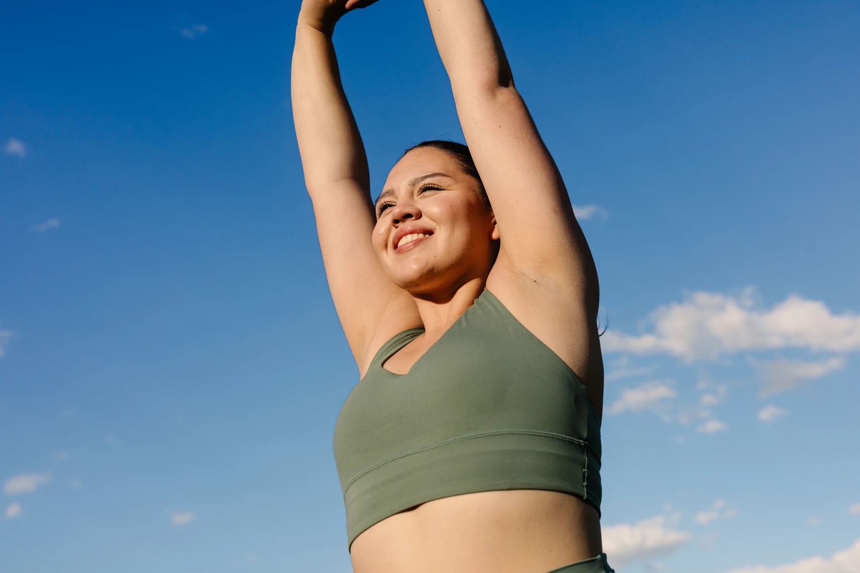 Smiling woman stretching both arms overhead against a blue sky