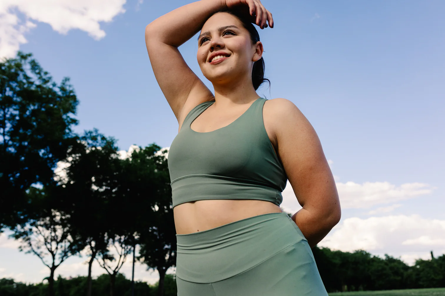 Smiling woman in a green sports top resting a hand on her head outdoors
