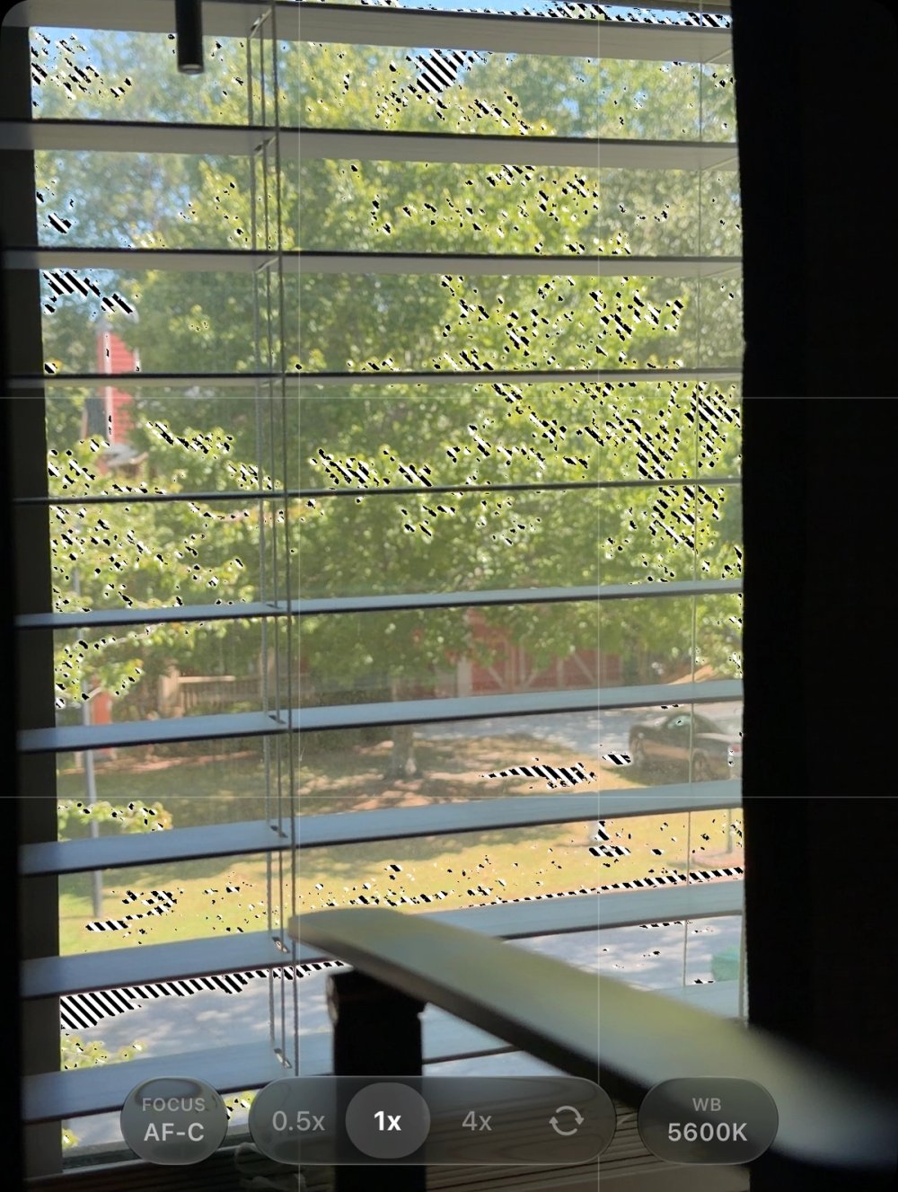 Zebra stripes mark bright regions in a camera preview of window blinds and an outdoor scene.