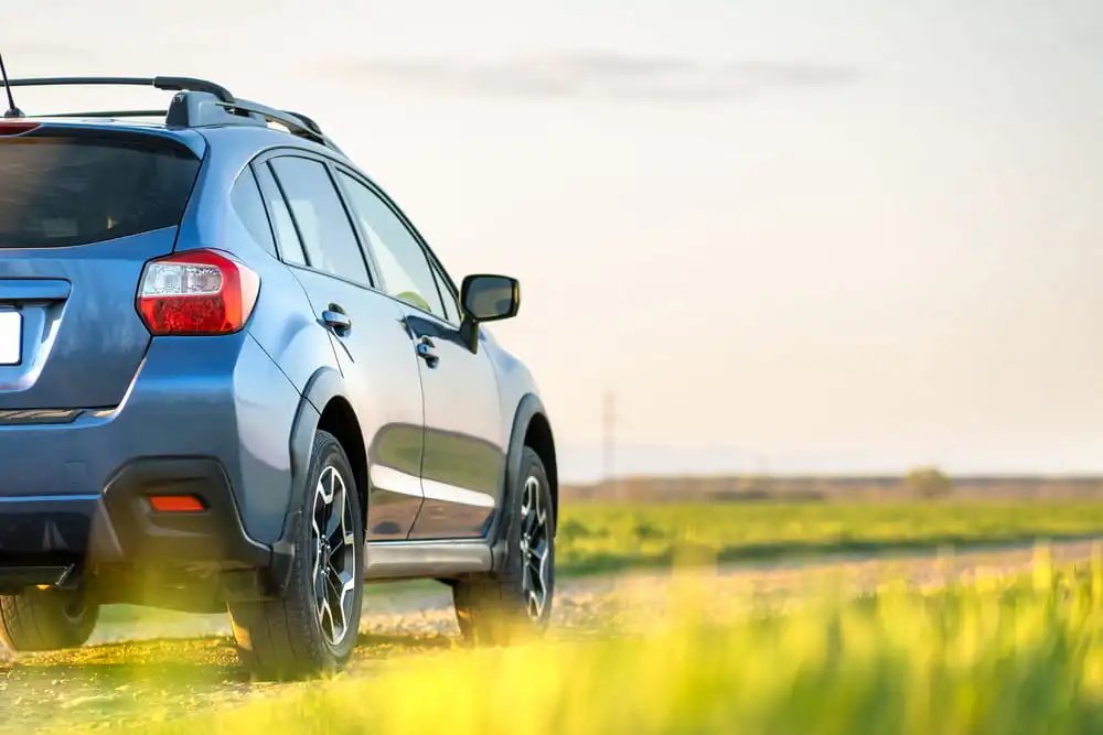 compact suv driving on gravel road surrounded by plain grass field