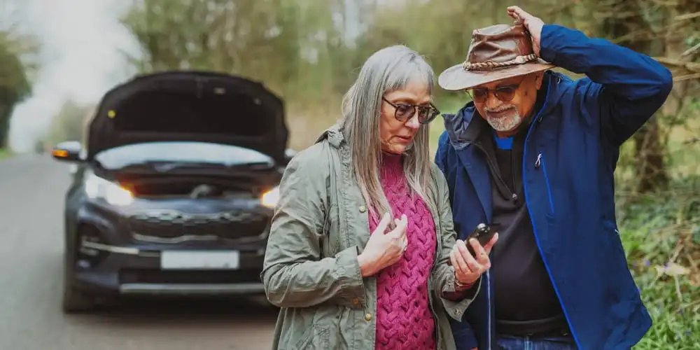 elderly couple broken down on side of road with car hood open