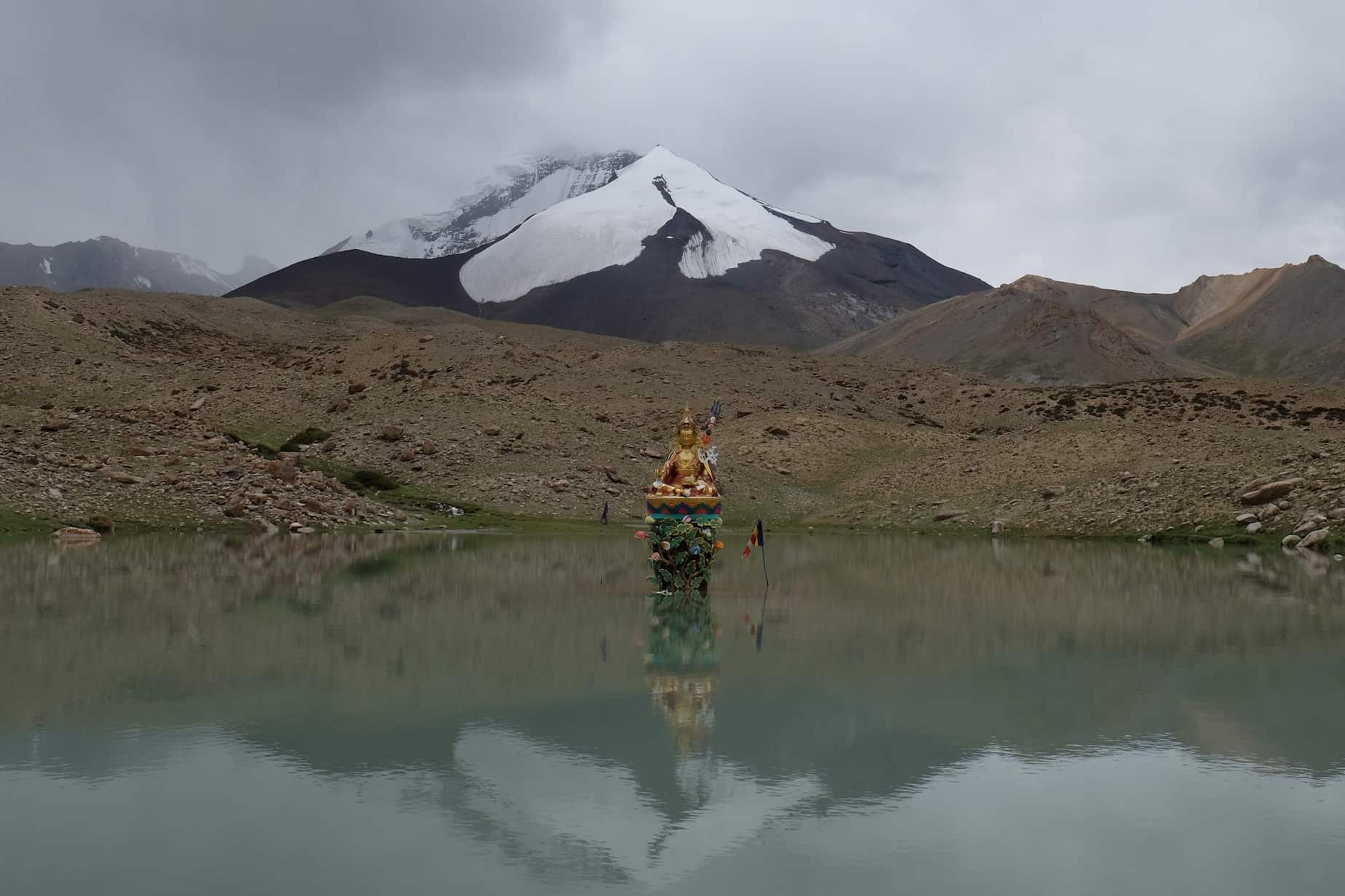 a golden statue sitting in a lake with a snow capped mountain behind