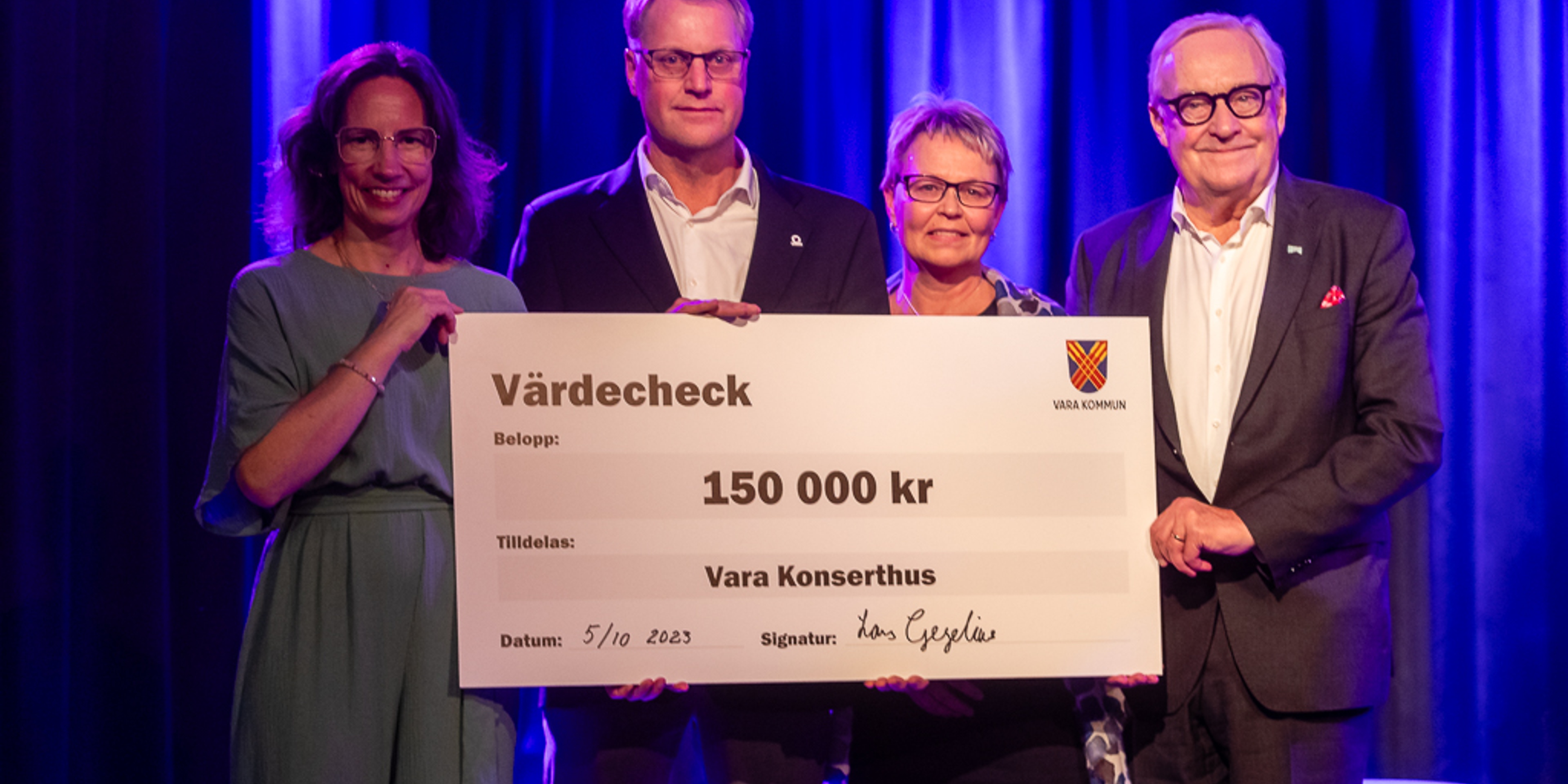 Bilden föreställer Vara Konserthus VDPetra Kloo, Kommunstyrelsens ordförande Lars Gezelius, Vara Kommuns kommundirektör Anna Cederquist och Vara Konserthus styrelseordförande Sture Carlsson leendes in i kameran med en stor check i famnen