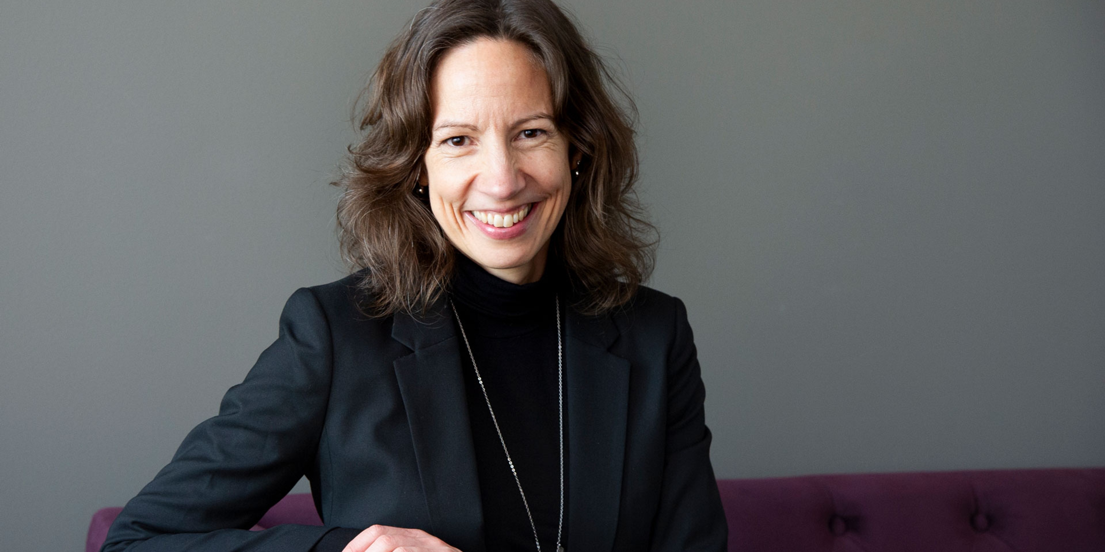 Petra Kloo sitter en lila soffa framför en grå vägg och ler in i kameran