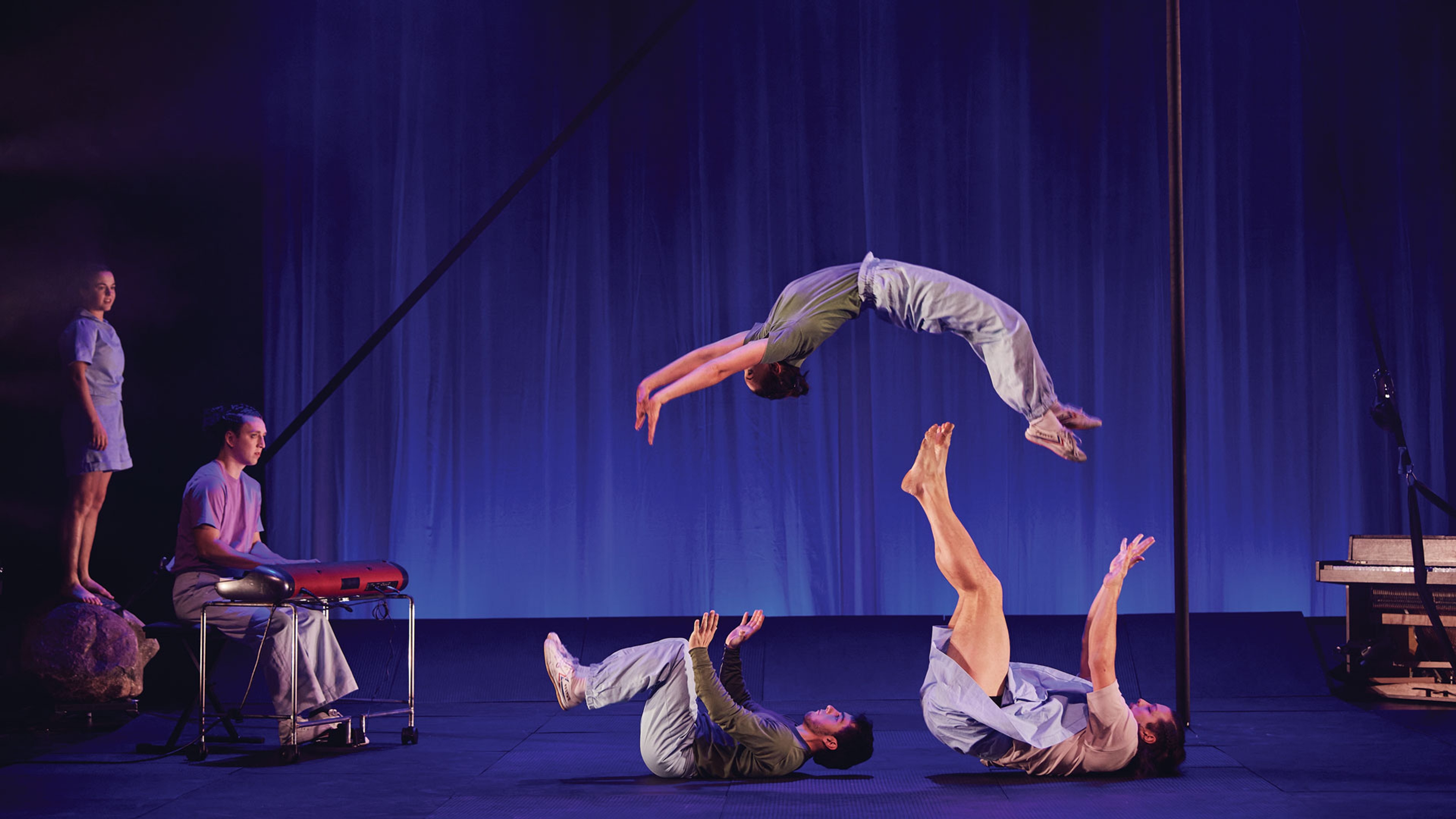 Personer ur föreställningen gör cirkuskonster och volter i luften på scenen