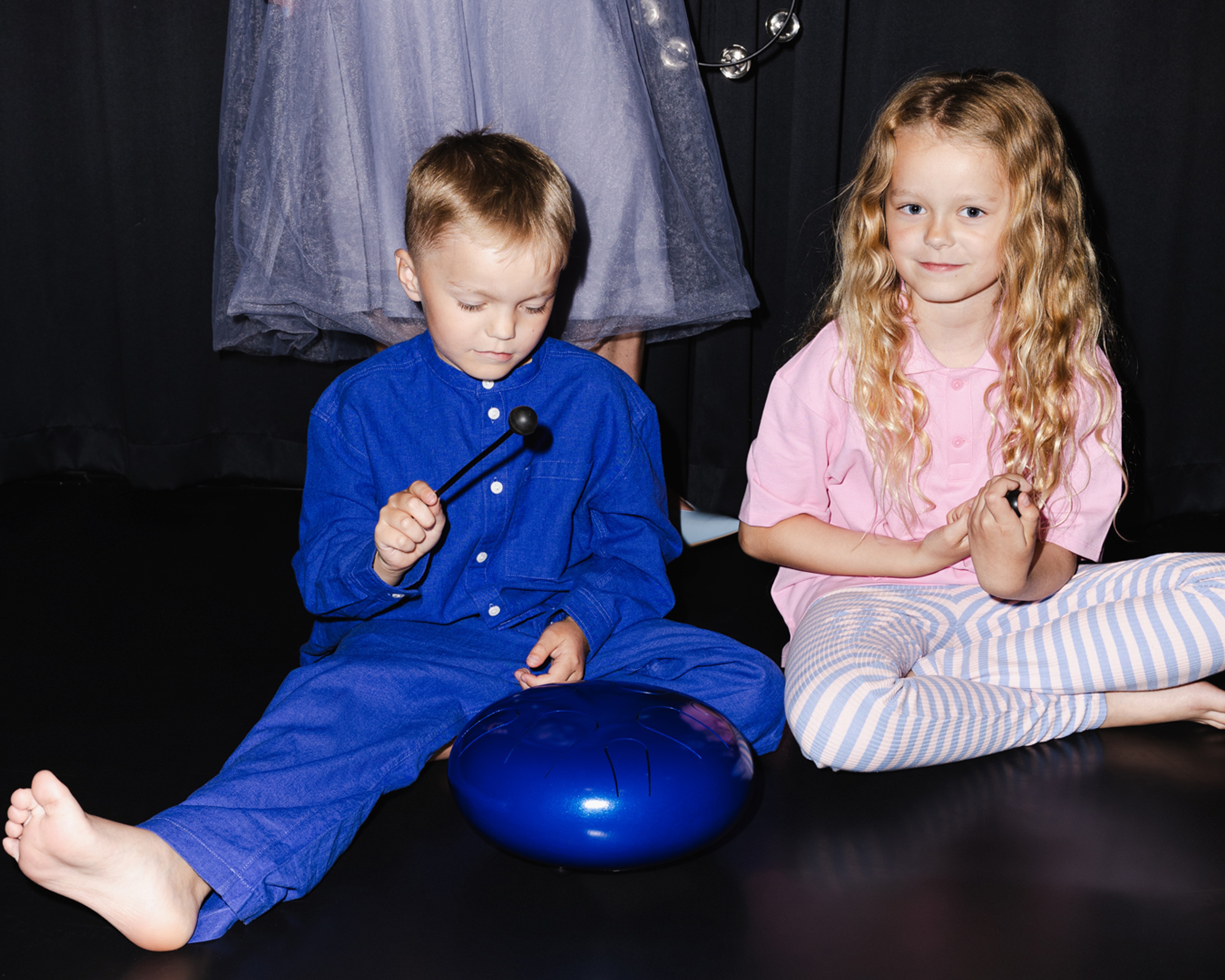 Två barn sittandes på golvet, pojken spelar instrument.
