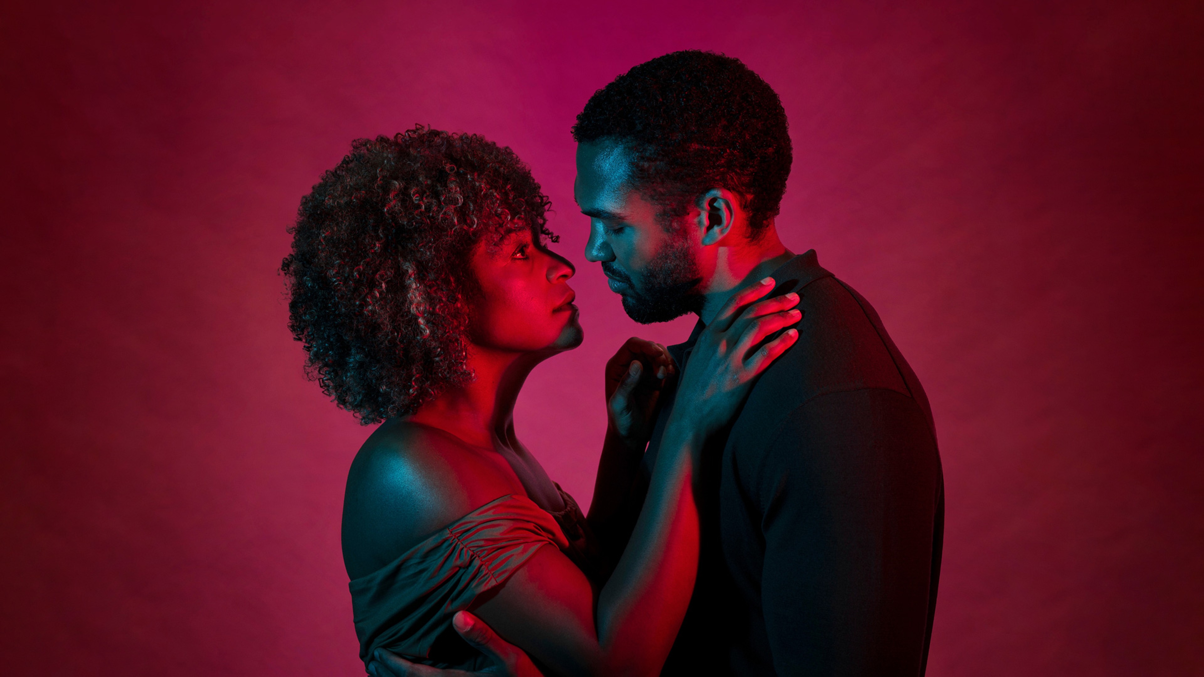 Två skådespelare kramar om varandra i rött ljus.