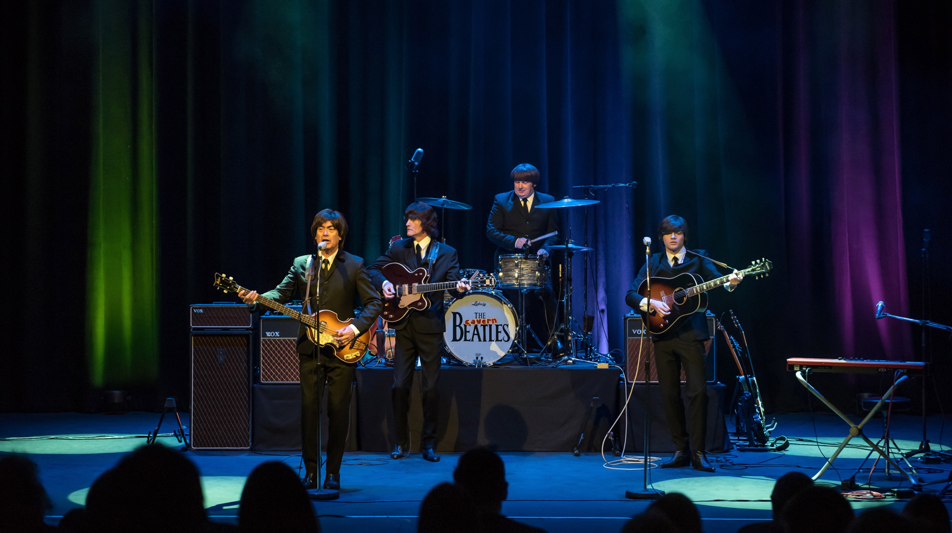 The Cavern Beatles står på scenen under spotlights och spelar inför publik