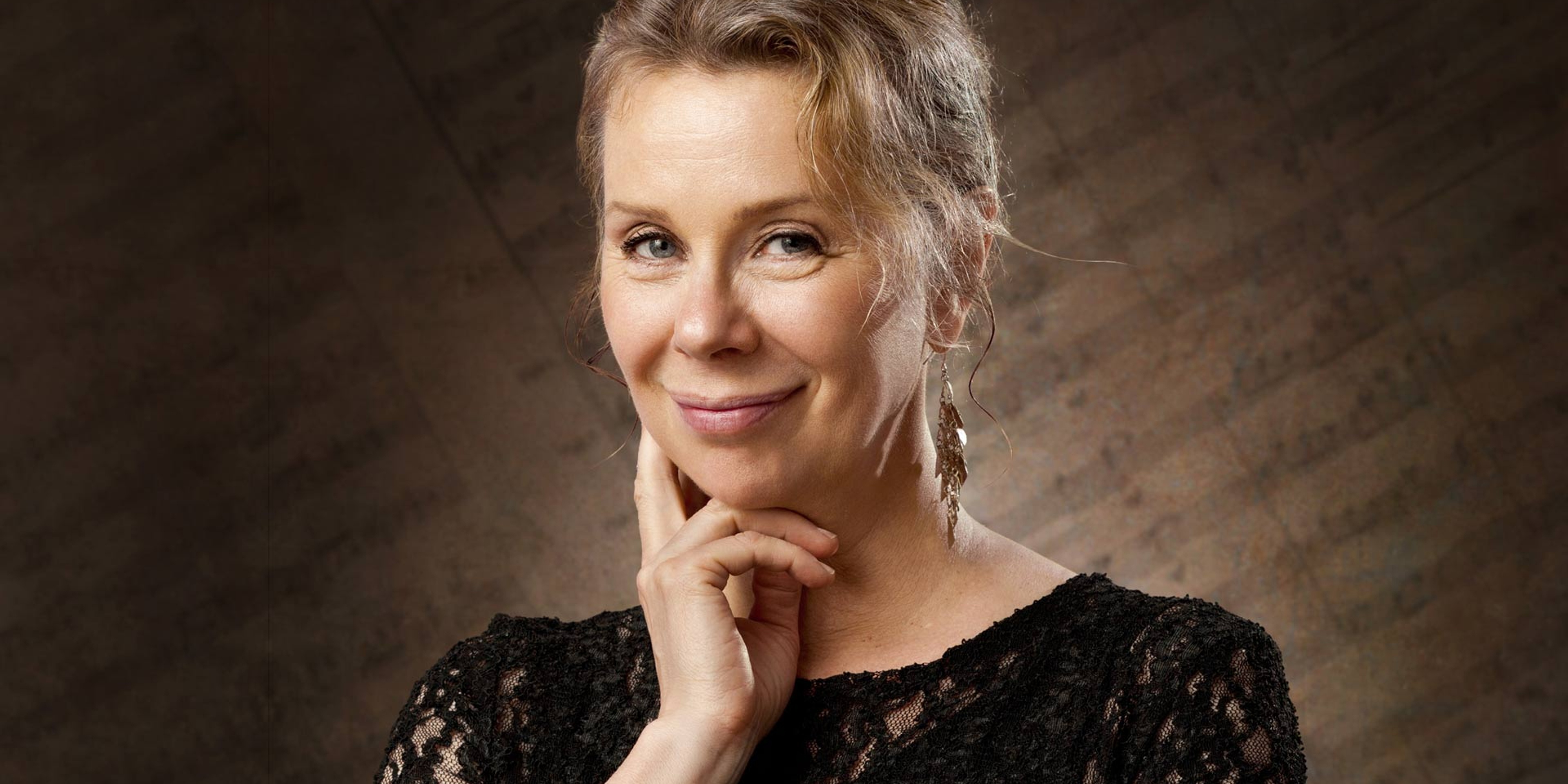 En leende Ann-Sofie Söderqvist med ena handen under hakan. I bakgrunden visas notblad.