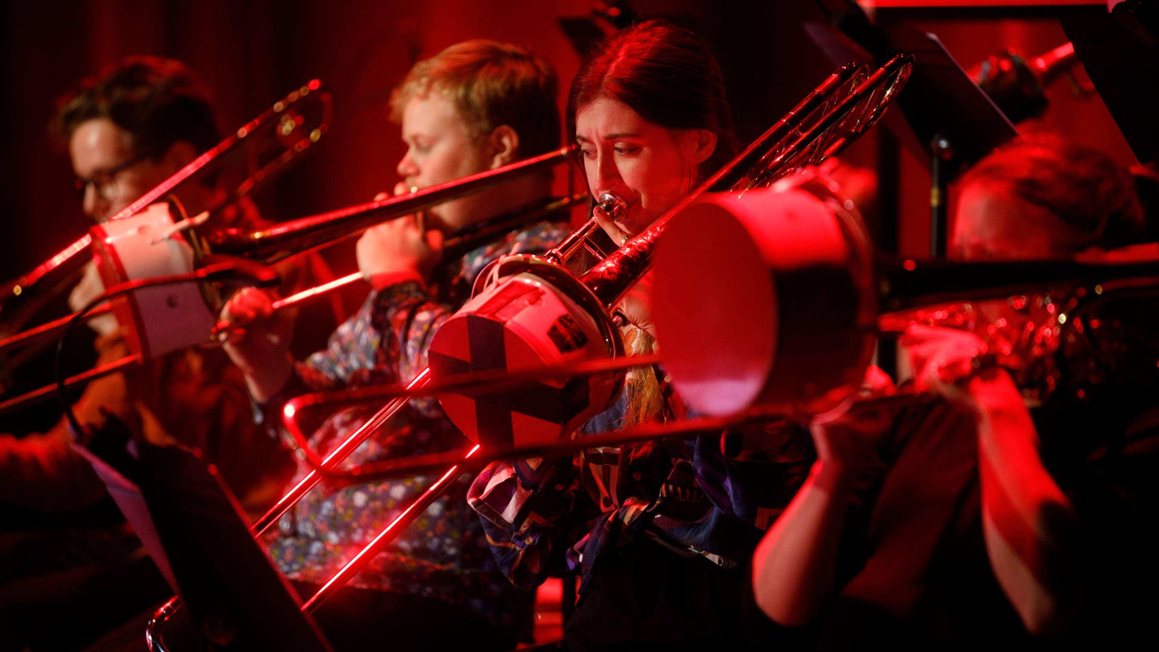 Unga blåsmusiker spelar tillsammans, fyra trombonister i fokus.