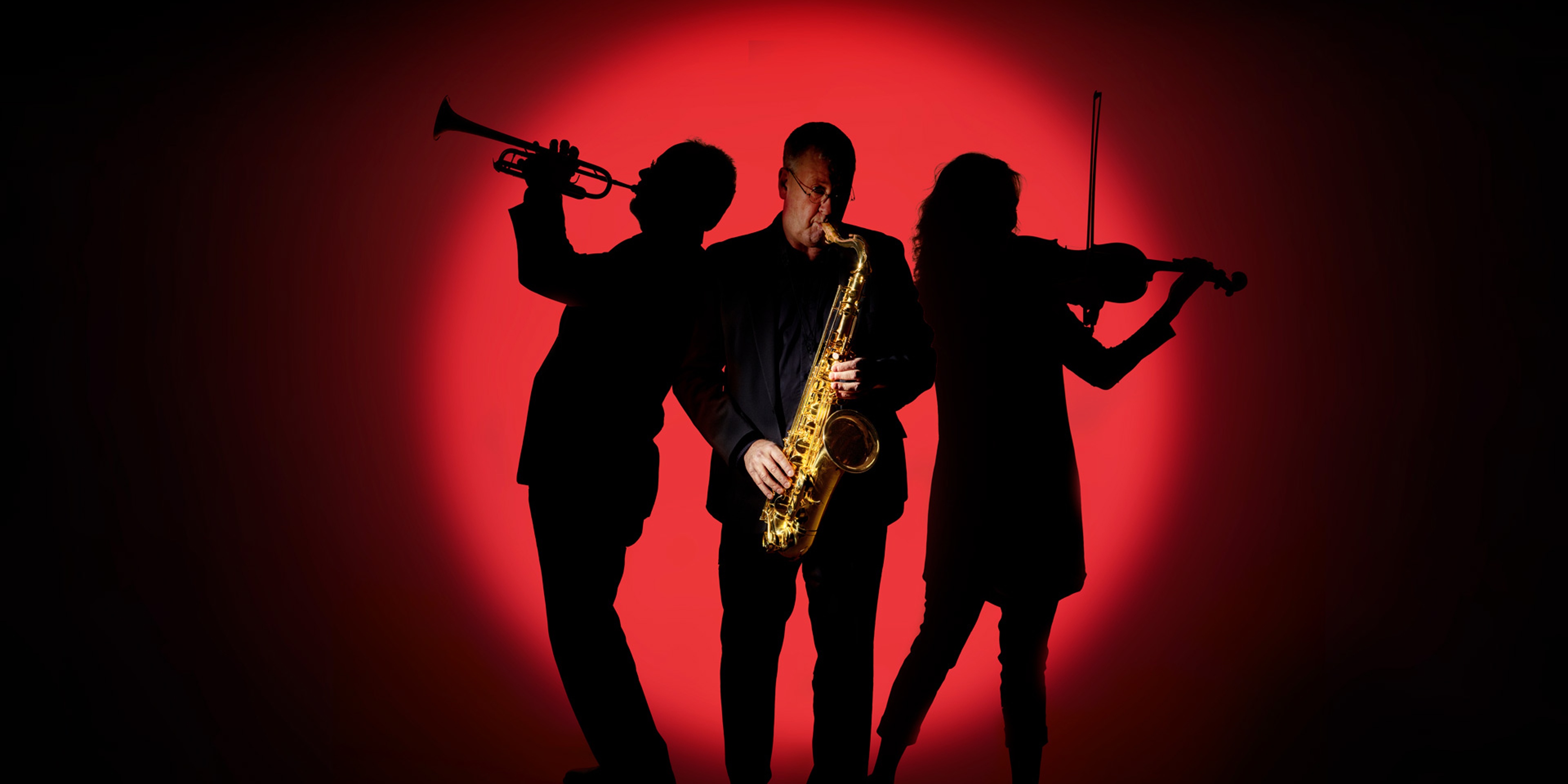 Tre musiker framför en röd bakgrund. En trumpetare till höger, en saxofonist i fokus i mitten och en violinist tillhöger.