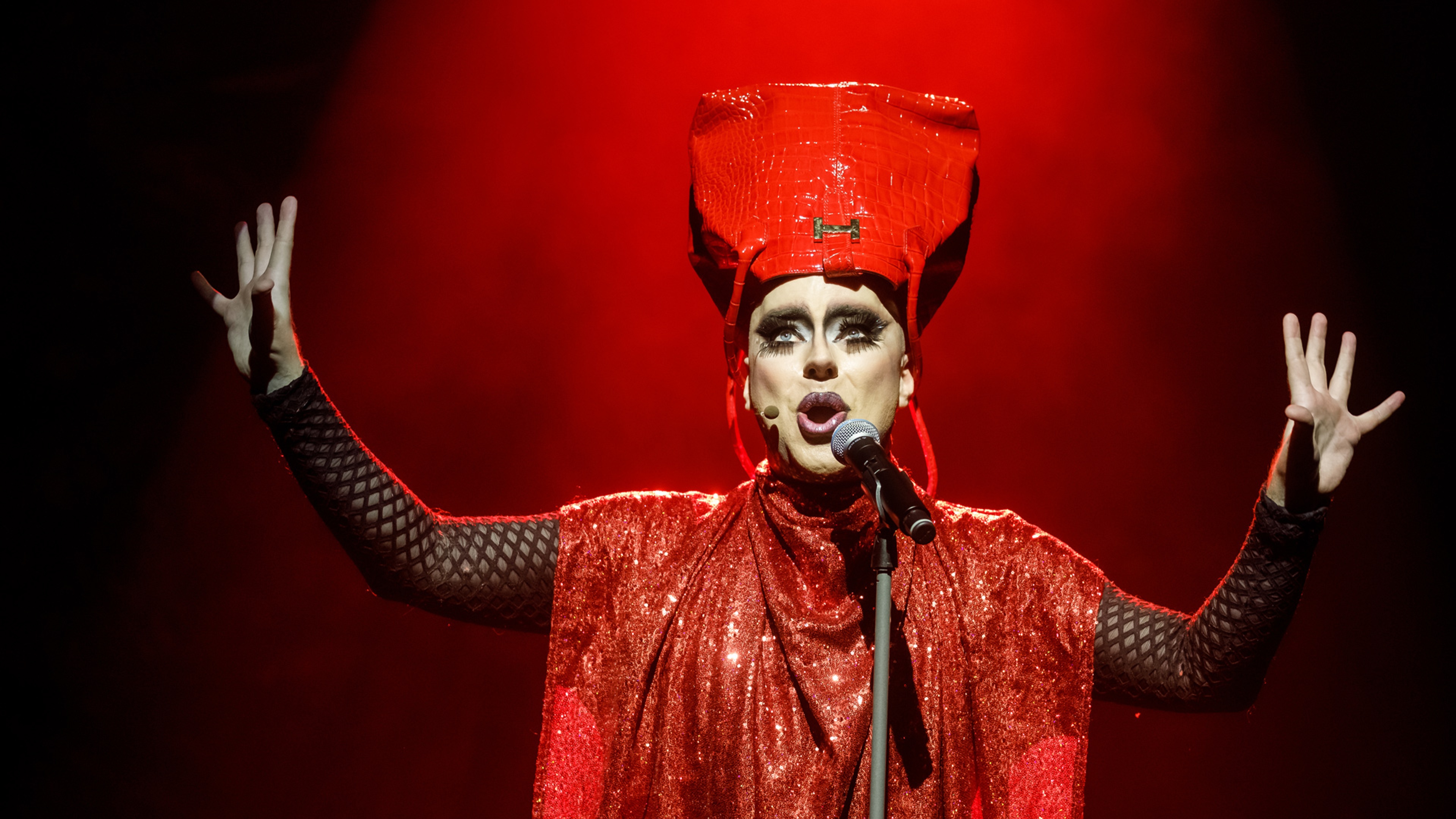 Robert Fux står helt rödklädd i drag med en röd väska på huvudet och händerna upp i luften mot en röd och rökig bakgrund