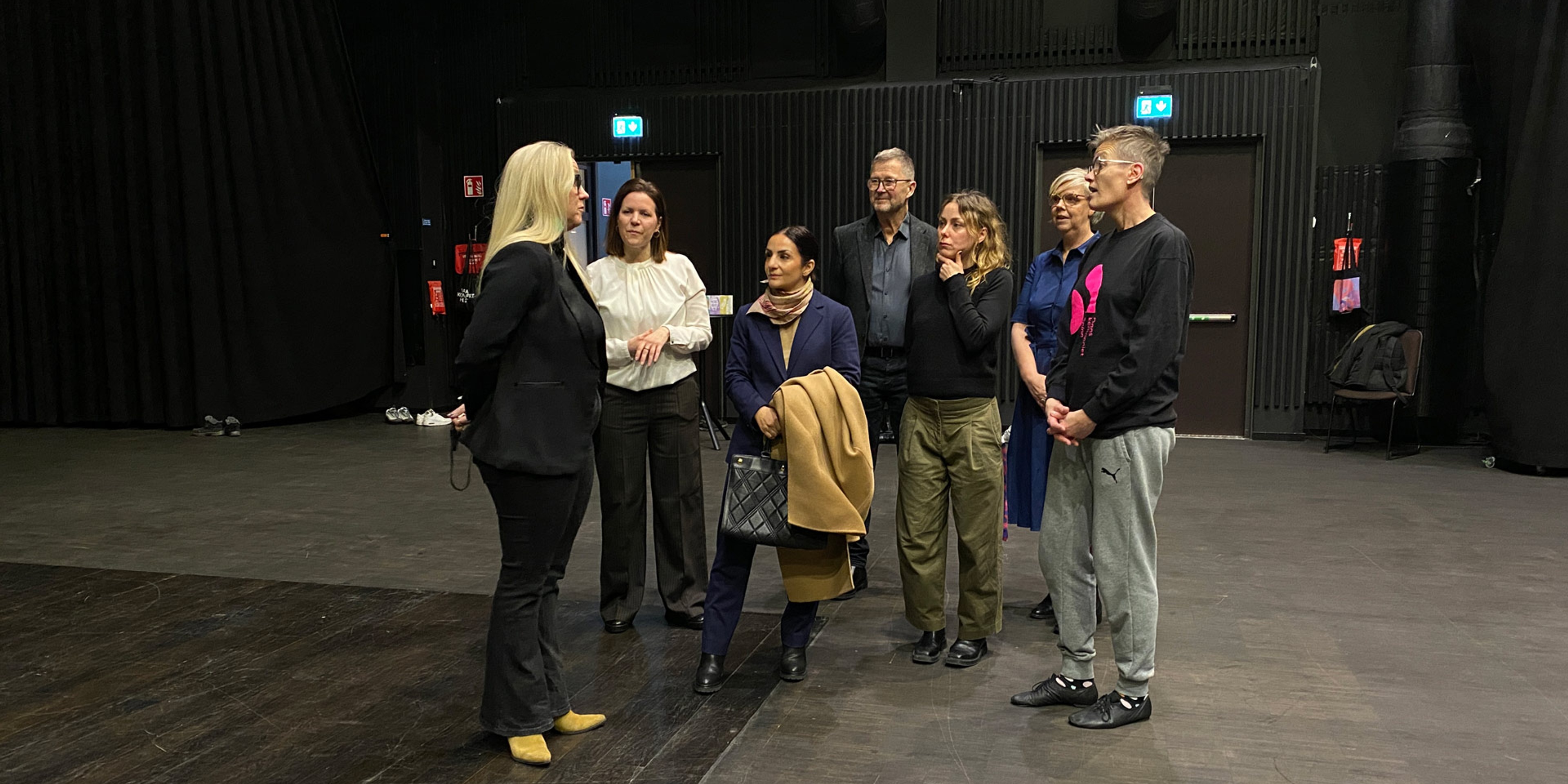 Sju personer står och pratar i blackboxen. Parisa Liljestrand står i mitten.