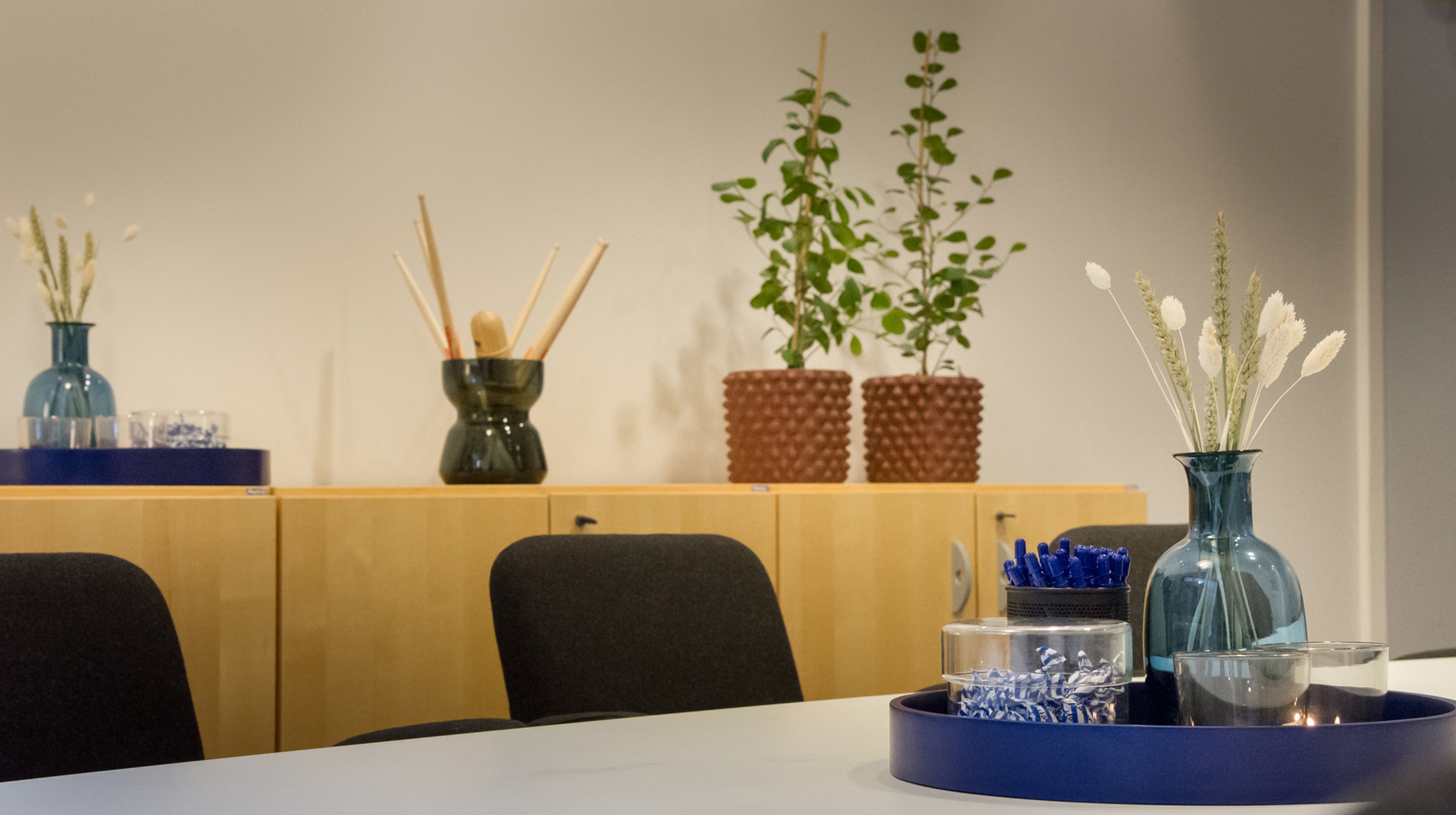 På konferensbordet står pennor, godis och en vas. På bänken bakom står blommor och en vas med trummpinnar.