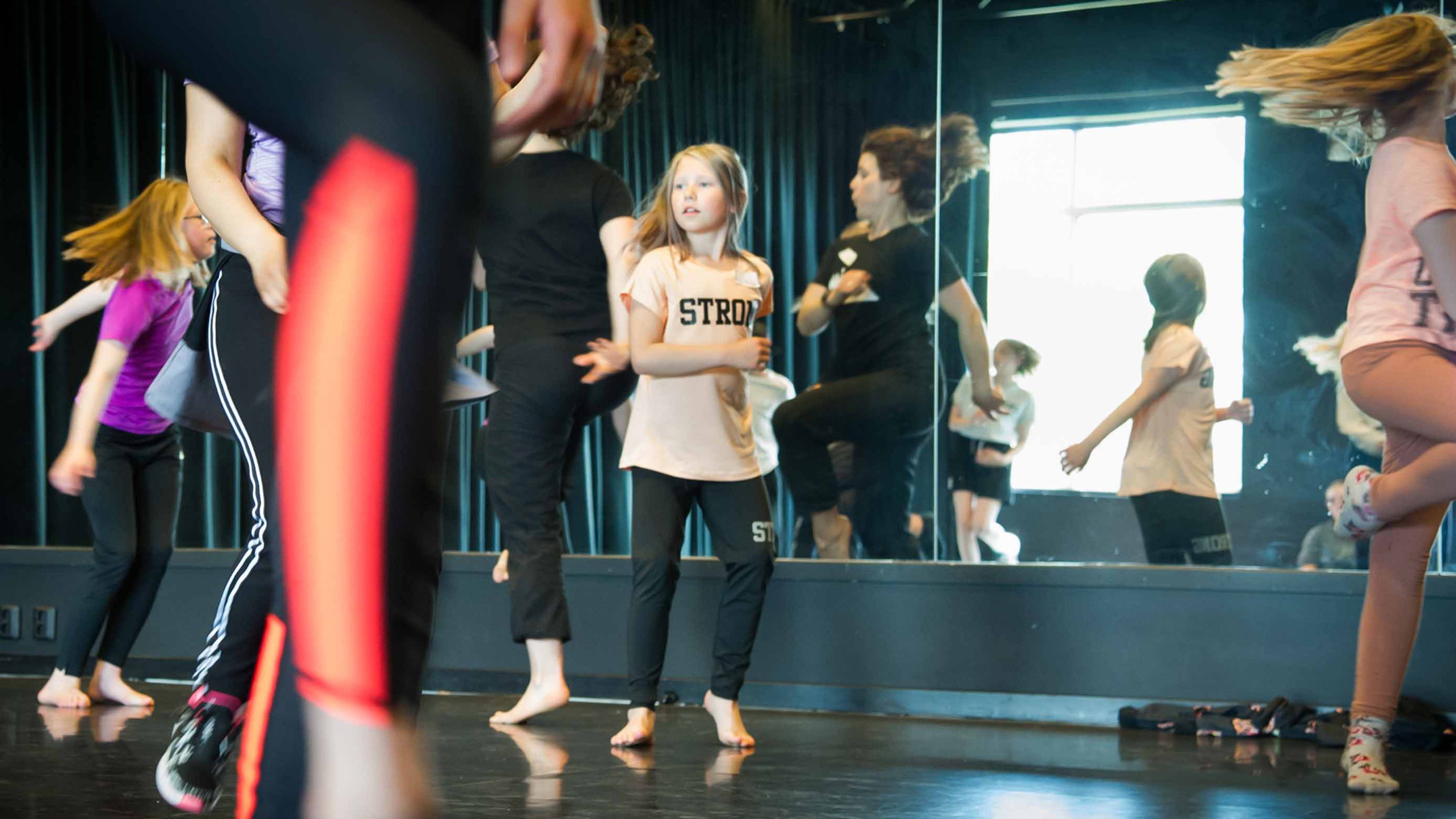 Barn som dansar framför spegel i en danssal.