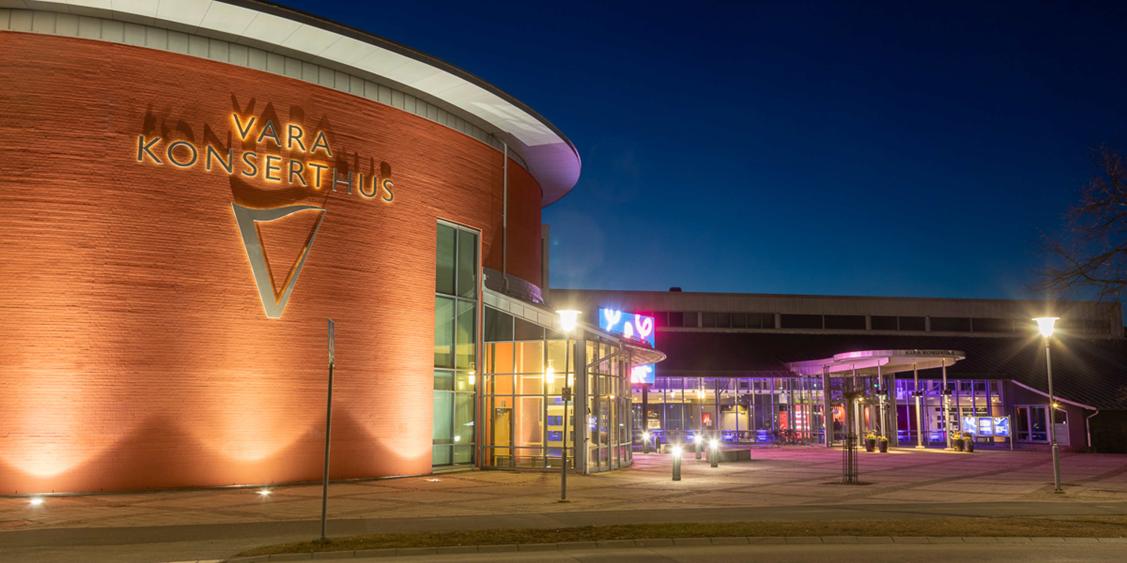 Vara Konserthus i mörker med tända spotlights som lyser upp och aktivitet inne i huset inför en konsert