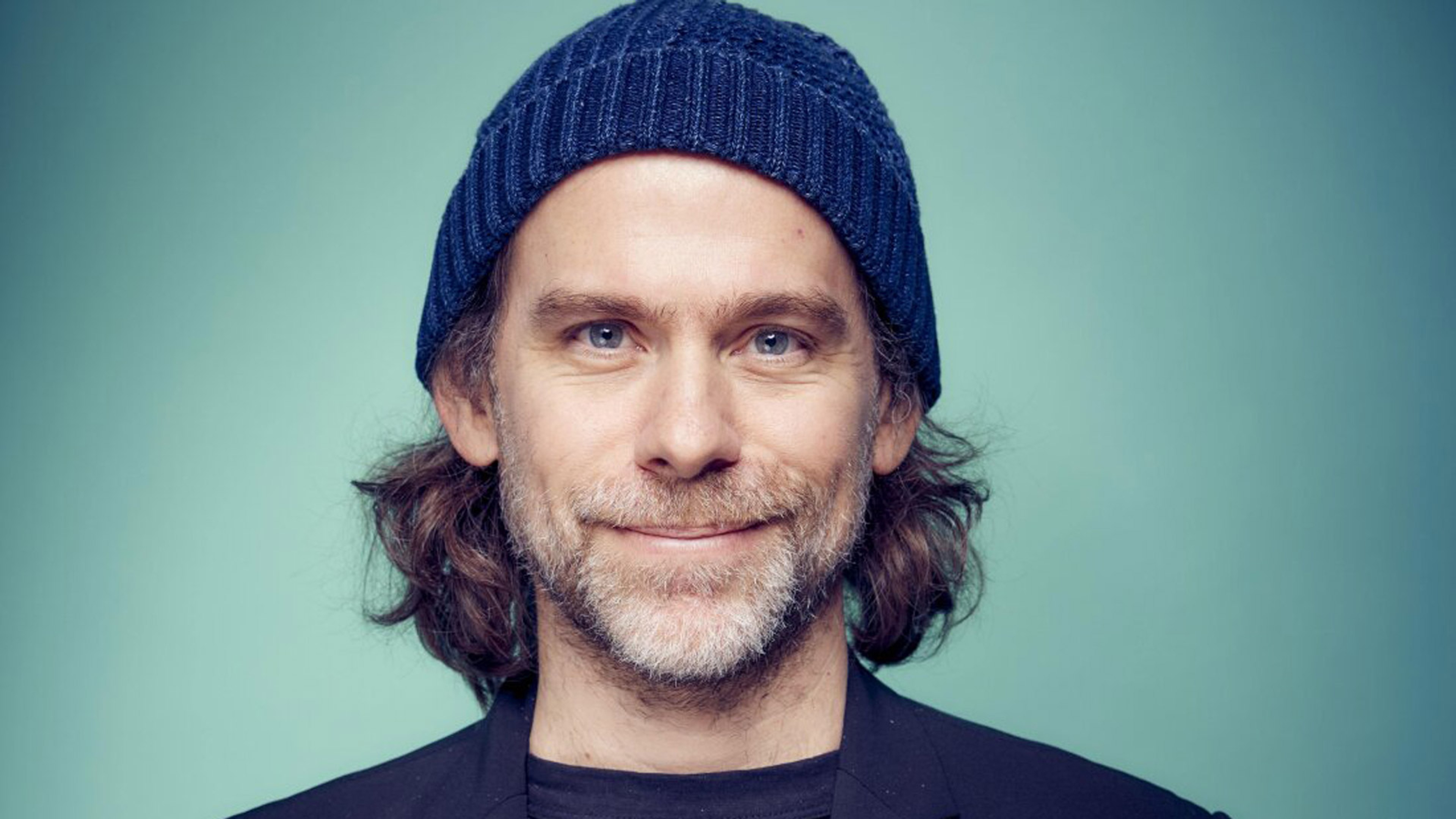 Bryce Dessner i mössa framför en grön vägg