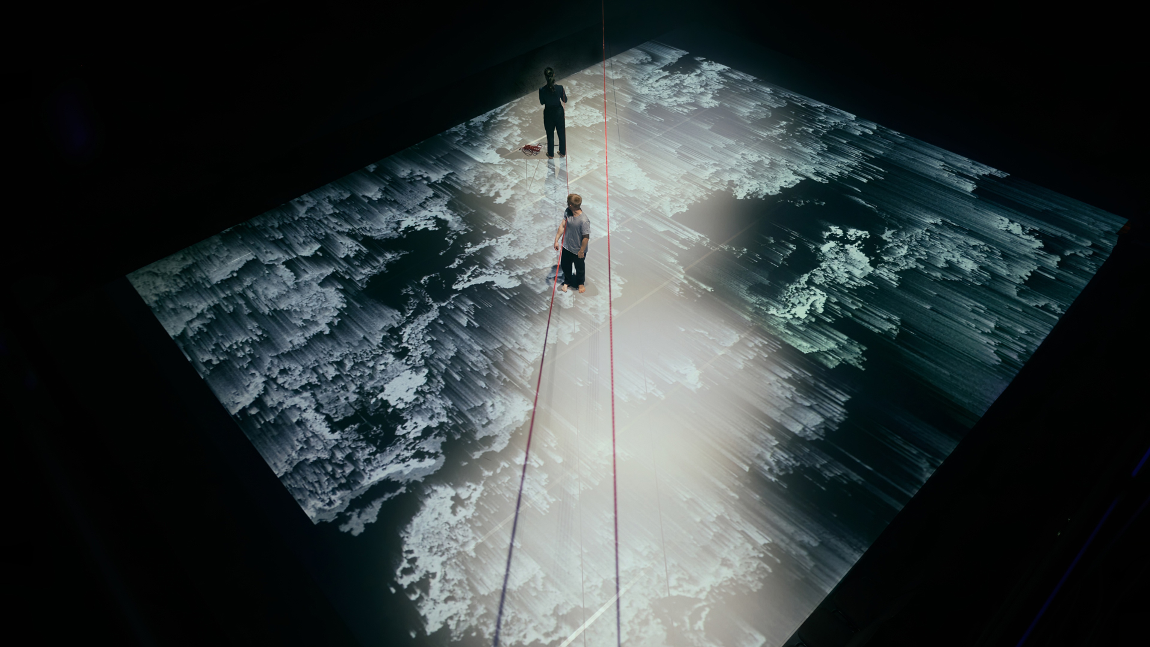 Två dansare på ett stort golv med grafiska projektioner. 