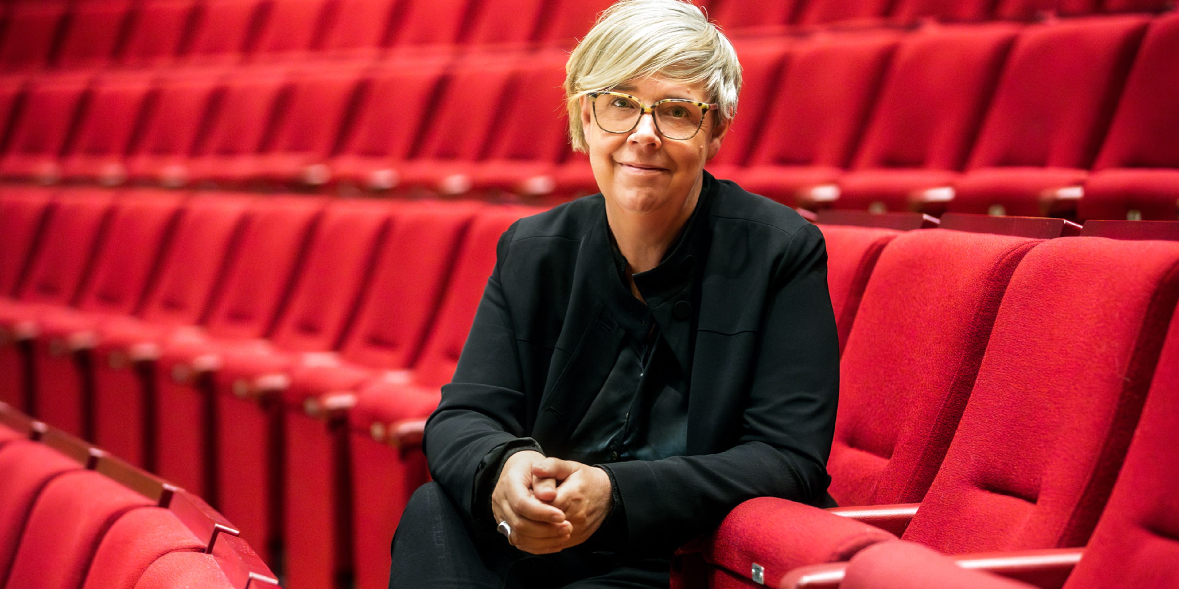 Karin Beckman sitter i röda stolar i konserthusets stora sal.