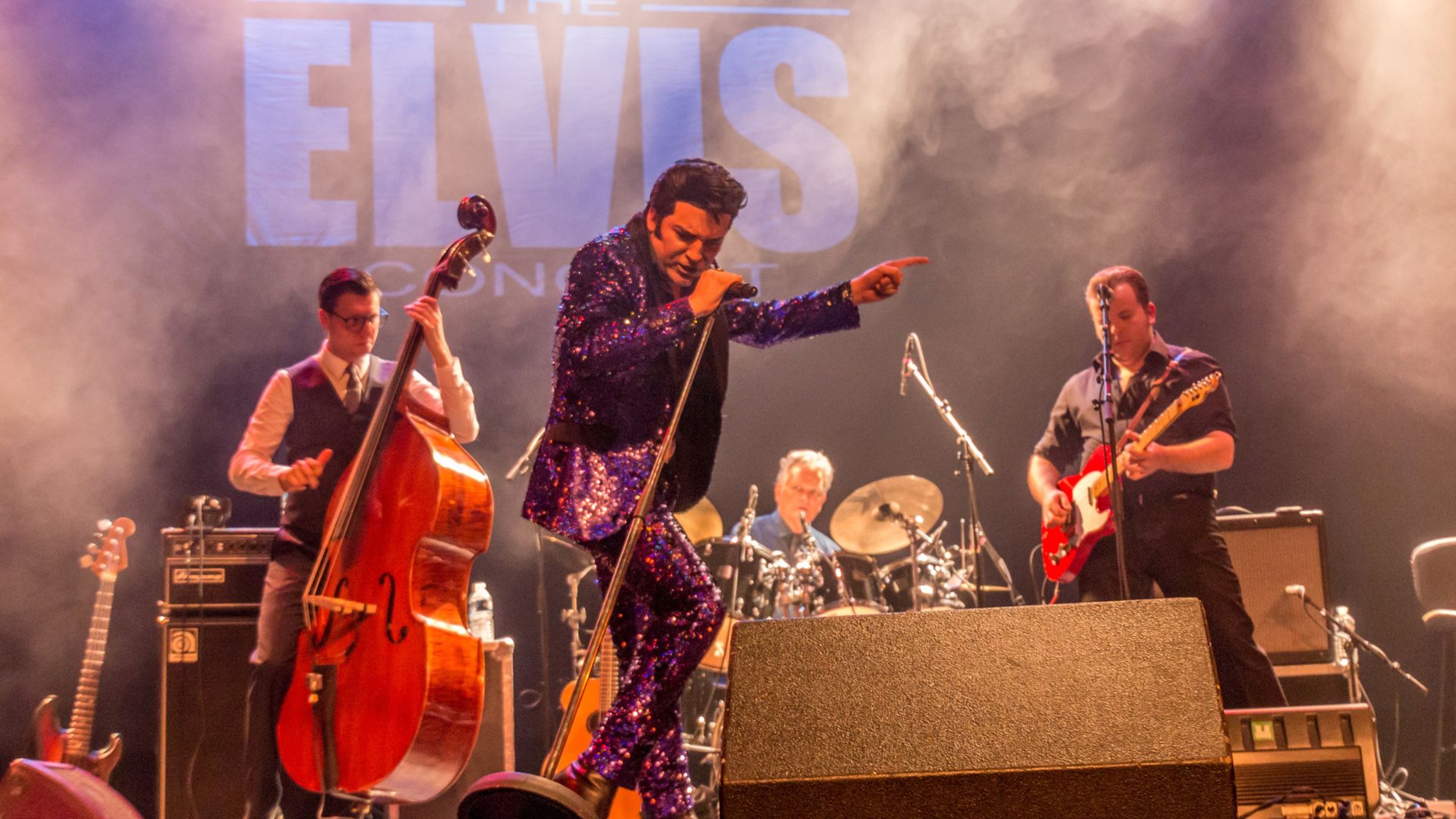 En sångare lik Elvis står på scenen i en lila, glittrig kostym.