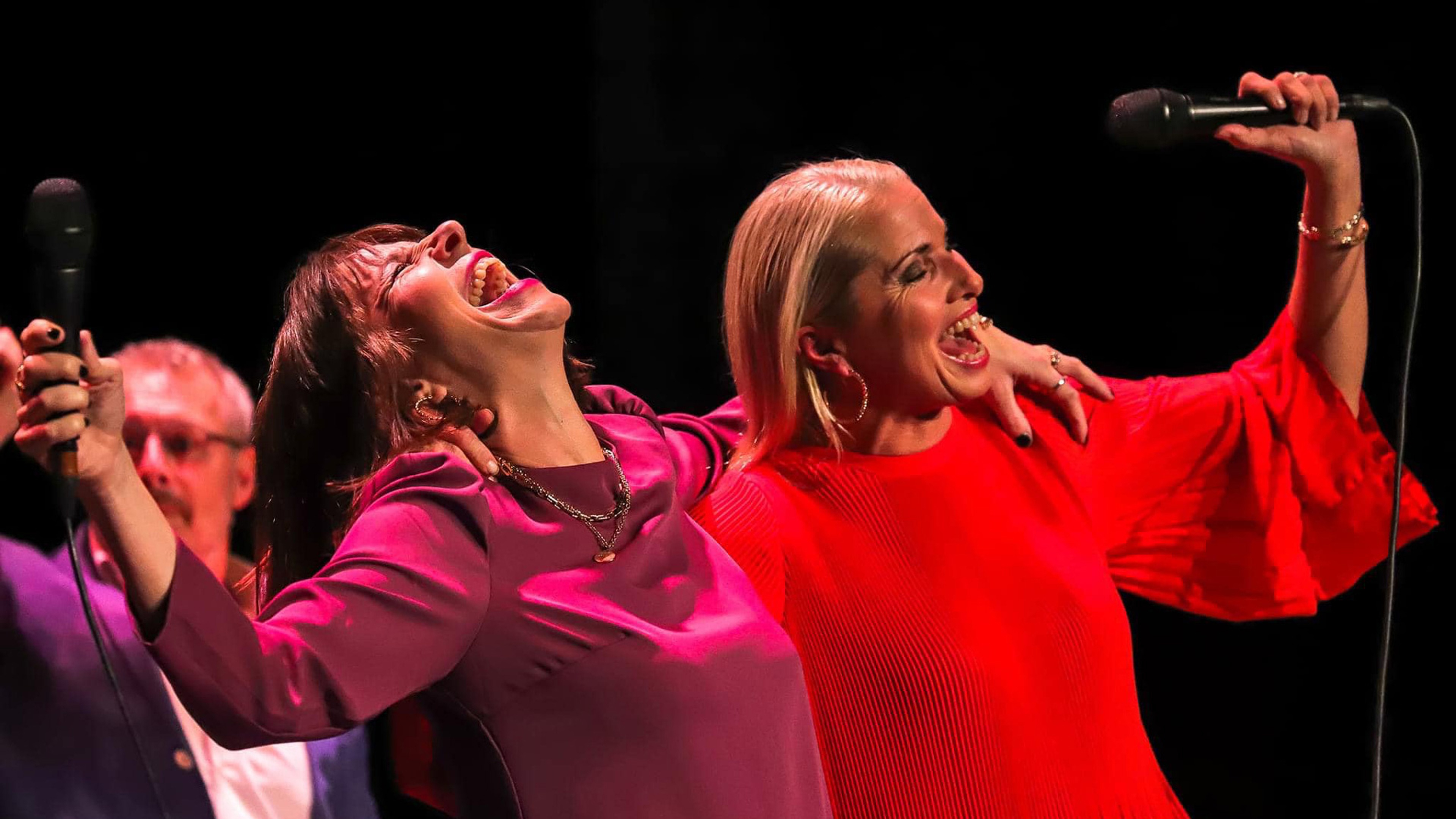 Två sångerskor skrattandes med mic i handen.