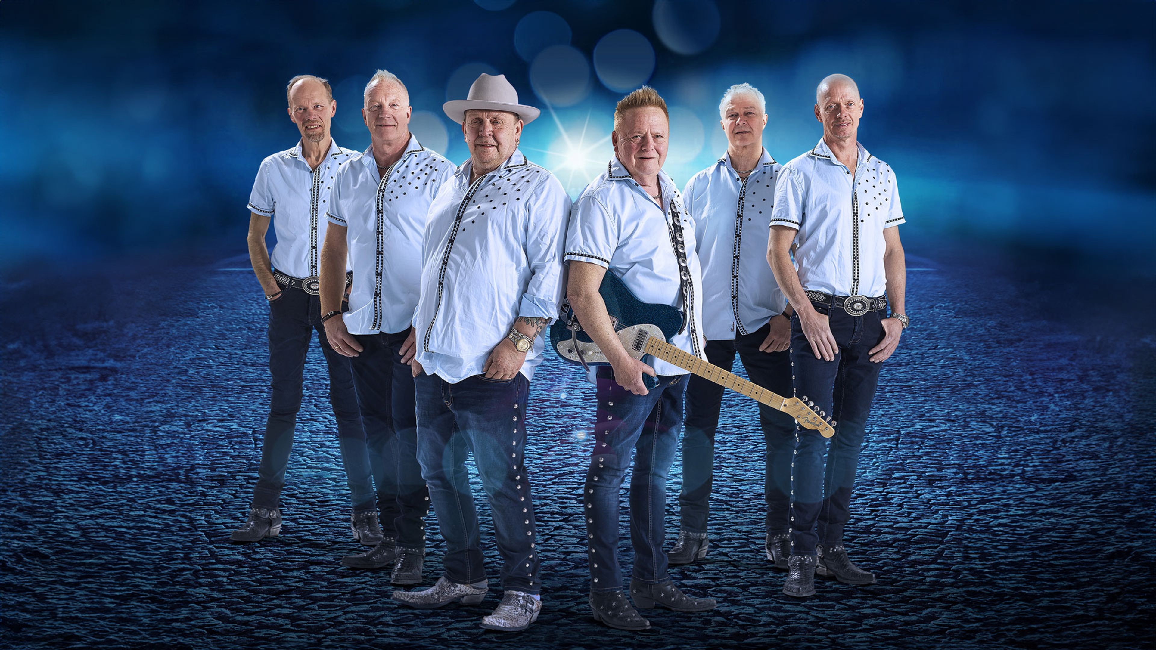 Bandet står uppställda i blå skjorta, jeans och boots.