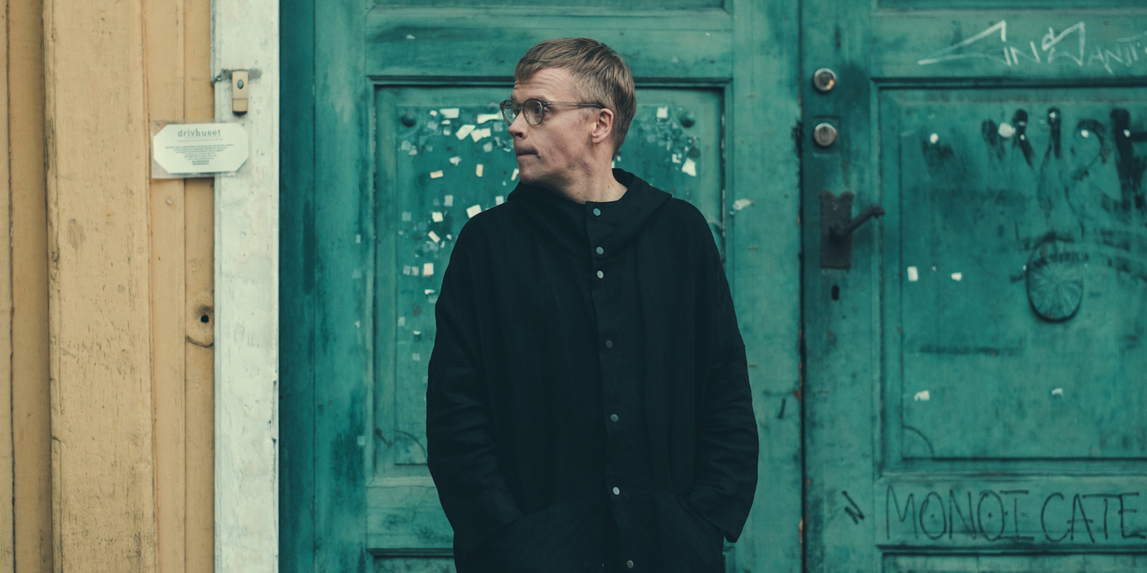 Pekka Kuusisto står framför en grön dörr på ett gult hus.