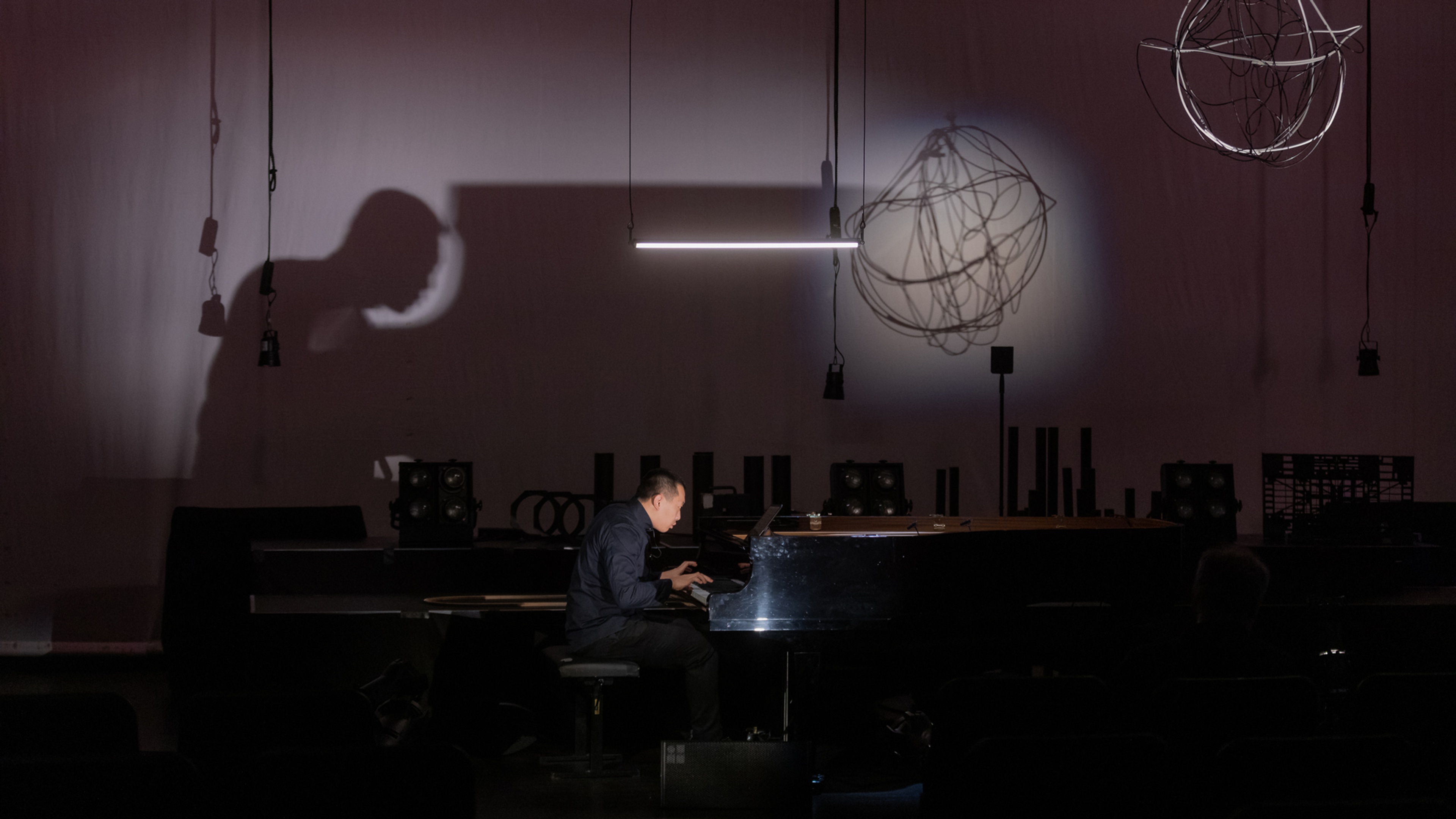 Pianist vid piano i mörkt rum, han lyses upp och skapar skugga på väggen bakom.