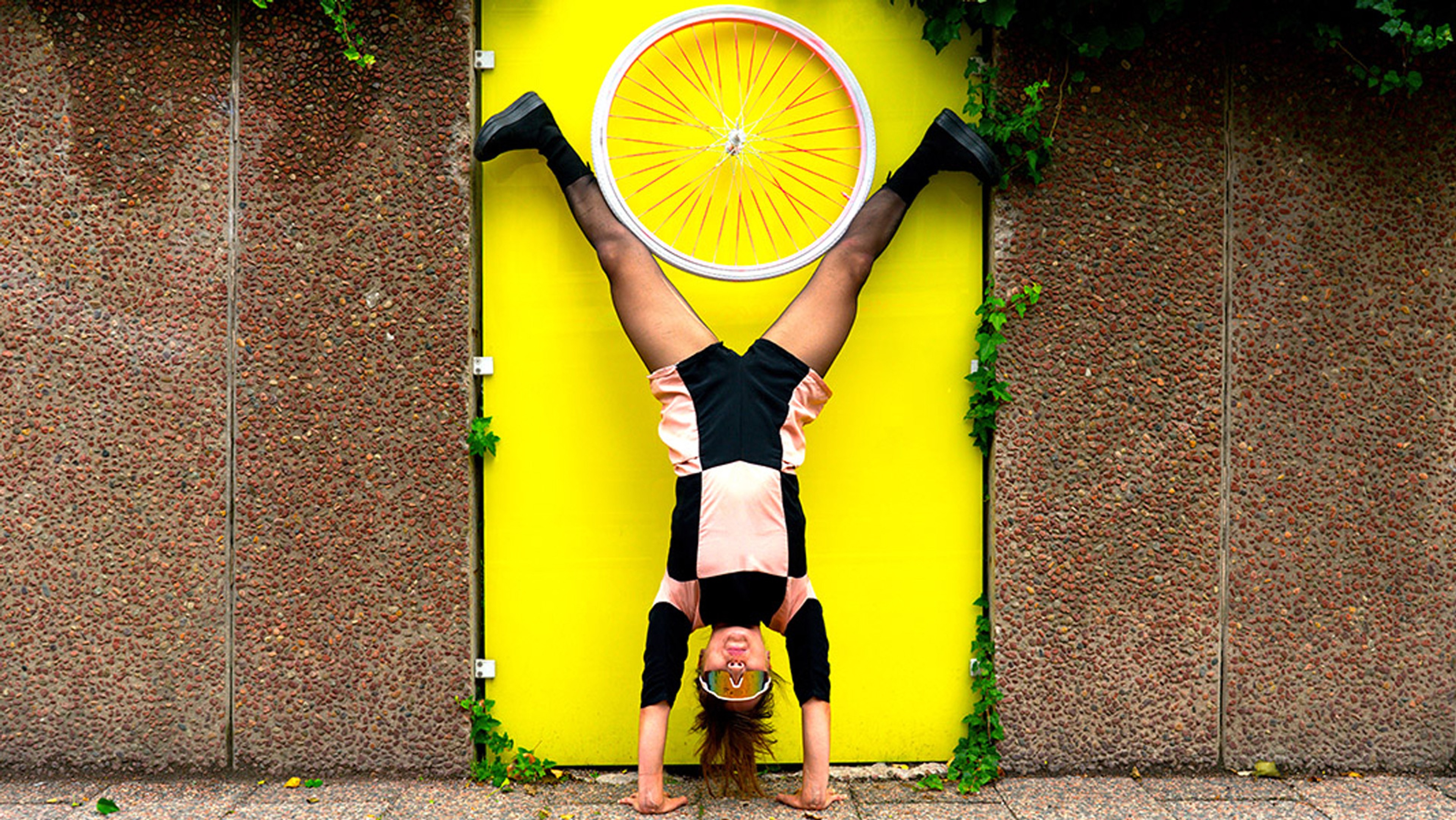 Kvinna står på händerna och håller ett cykelhjul med benen. 