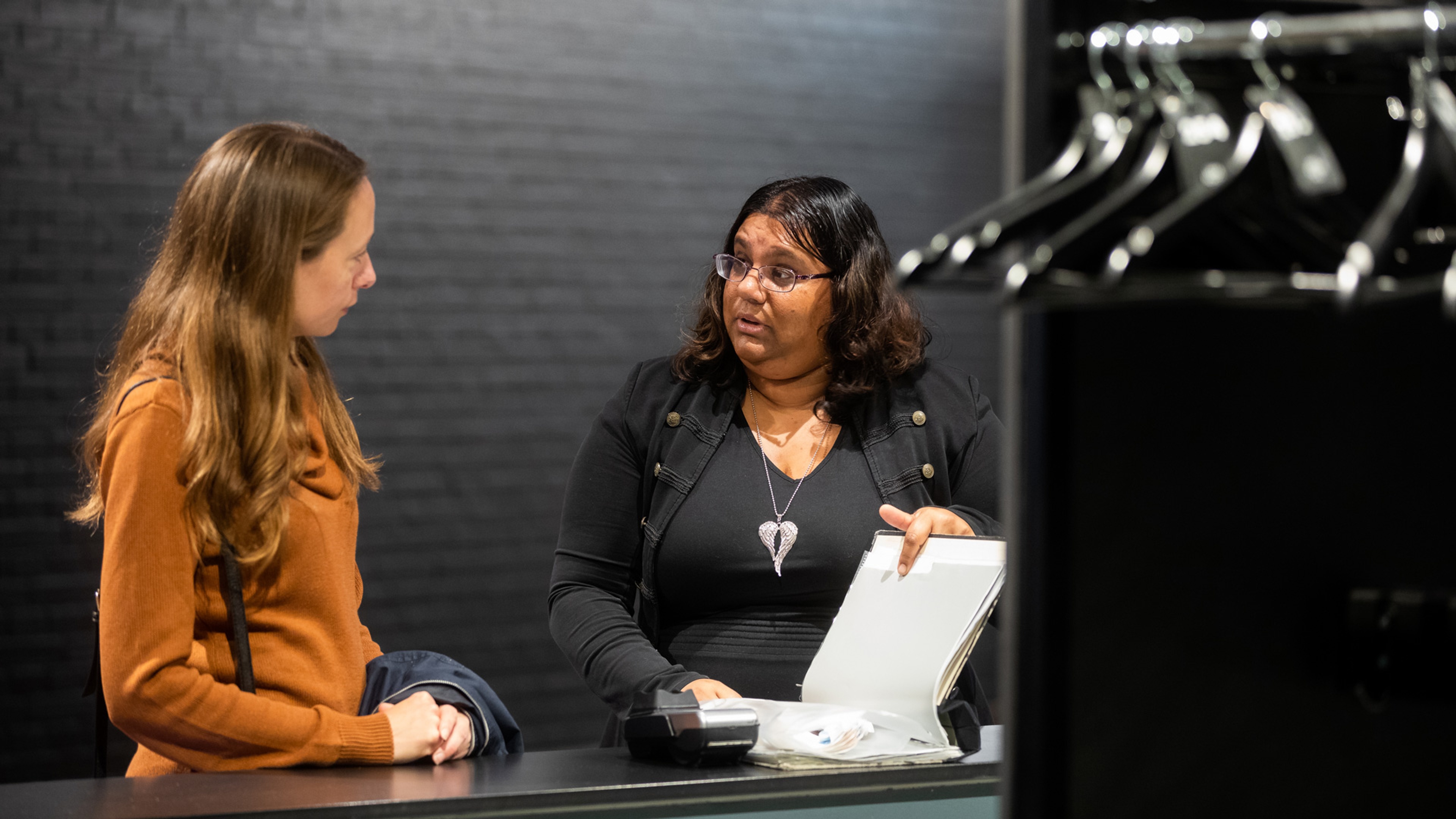 Två personer står och pratar med varandra. Den ena personen håller i en uppslagen pärm.