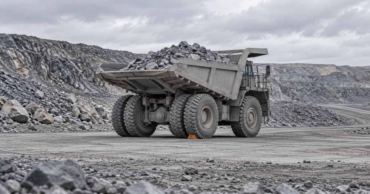 A loaded haul truck stands idle beside a dusty mine road with a small wheel chock behind its tire.