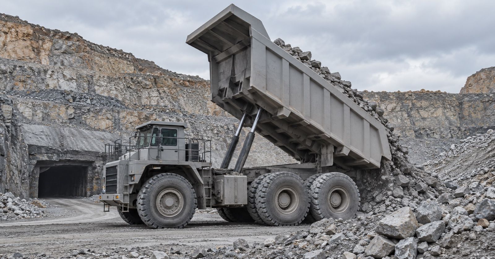 A haul truck tips broken rock onto a mine stockpile near a tunnel entrance.