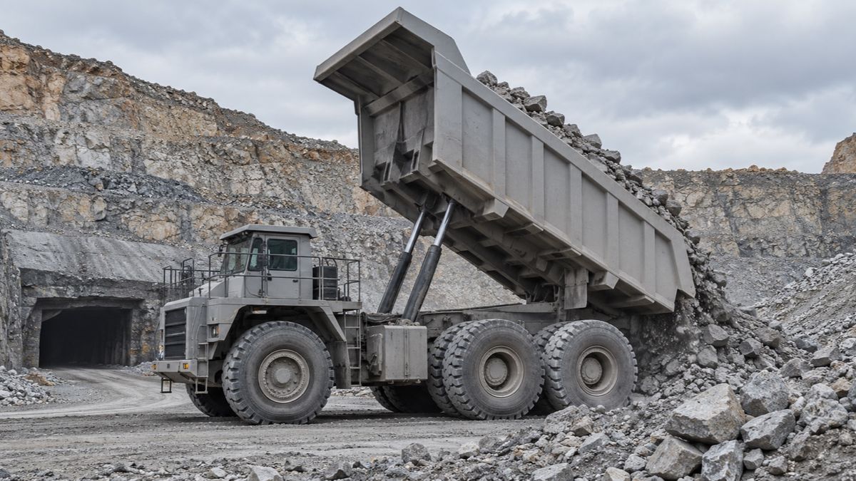 A haul truck tips broken rock onto a mine stockpile near a tunnel entrance.