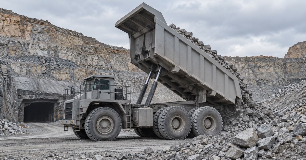 A haul truck tips broken rock onto a mine stockpile near a tunnel entrance.