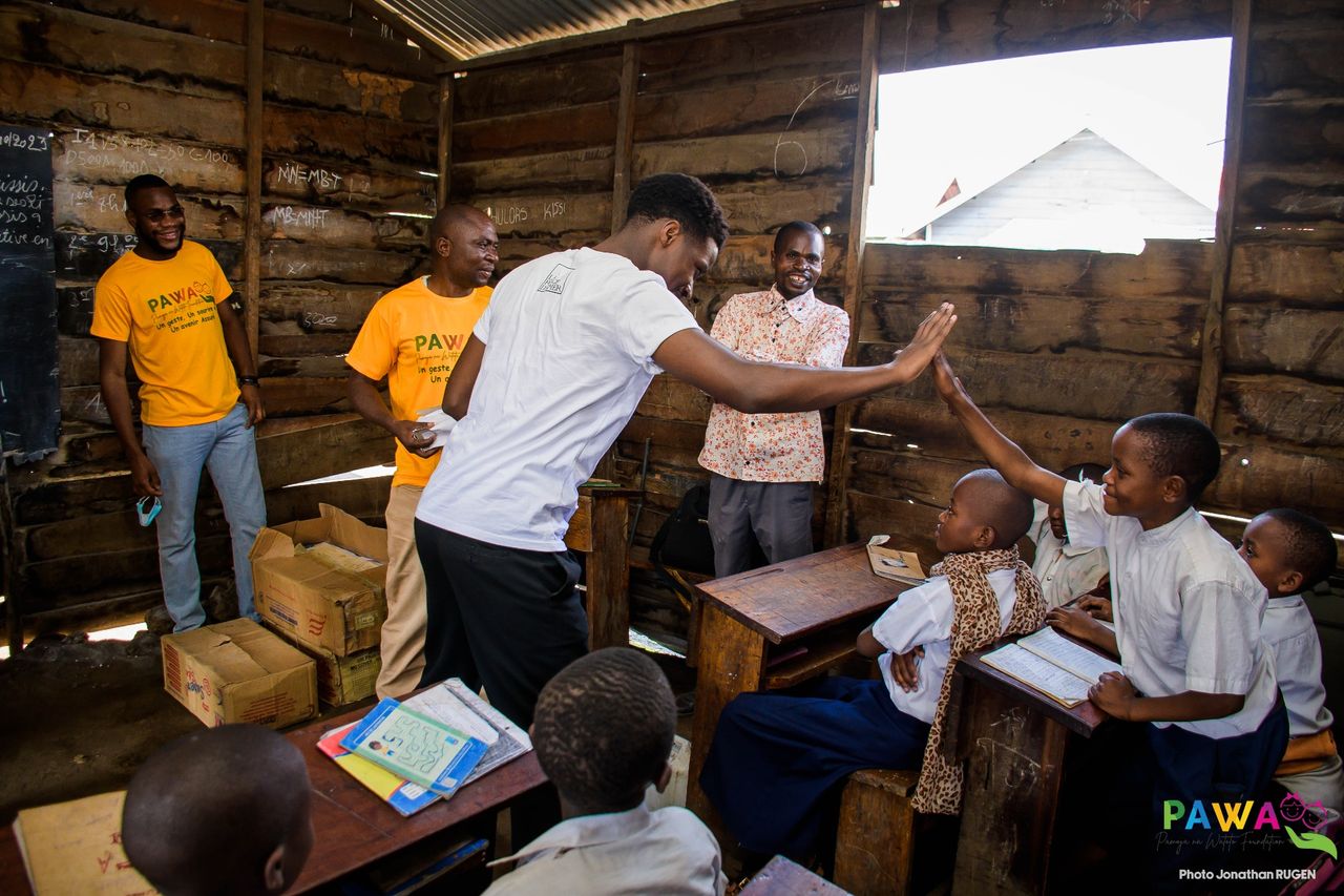 Bénévole saluant un écolier dans une salle de classe en planches, à Goma