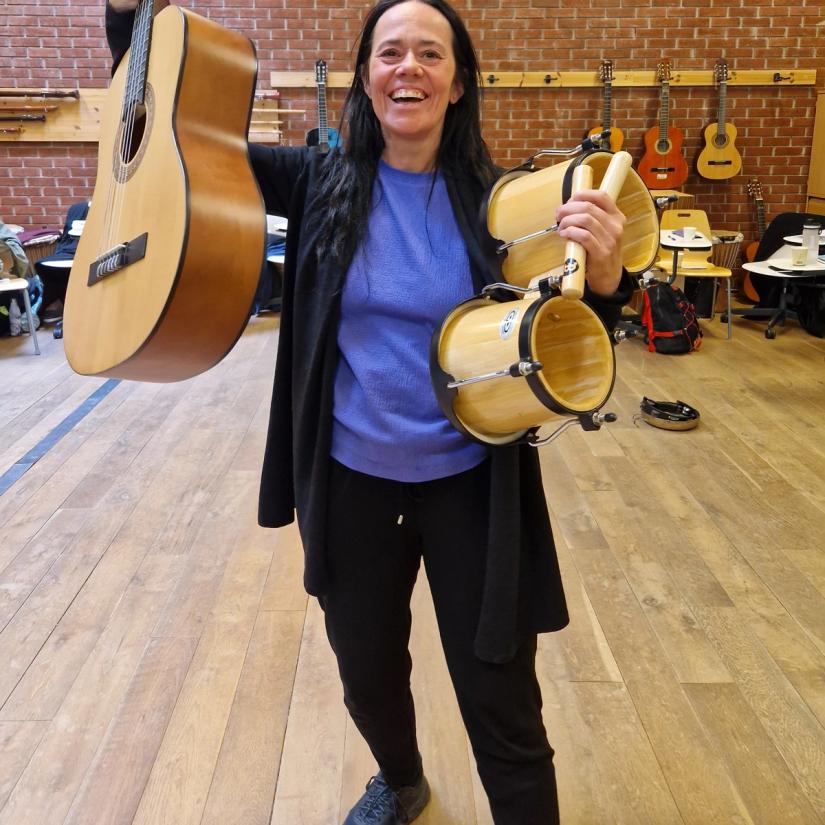 Vi ser en smilende deltaker på kurs med Lise Lotte Berg, med gitar og tromme i hendene.