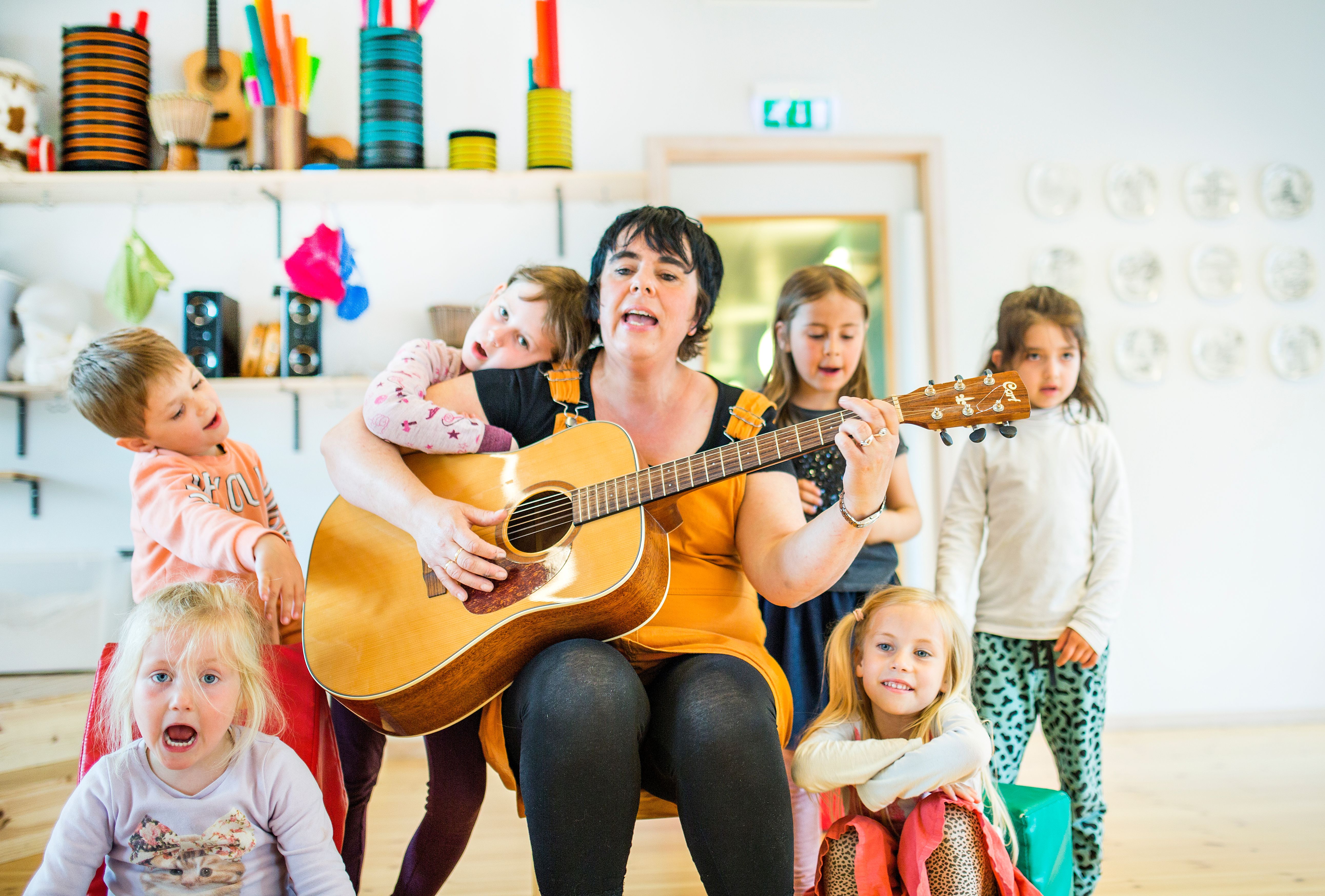 En syngende barnehageansatt omringet av glade barn
