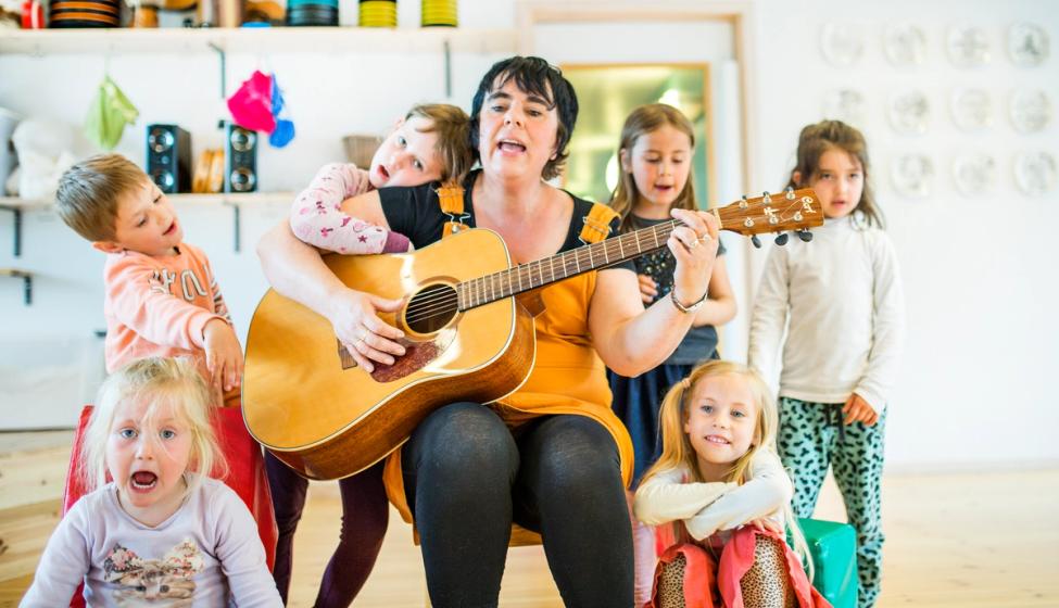 En syngende barnehageansatt omringet av glade barn