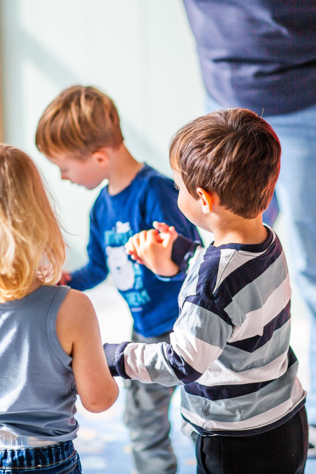 Bilde av tre barn som holder hender i en ringlek i barnehagen