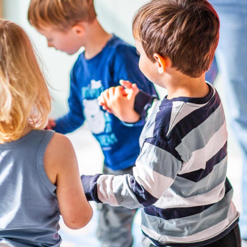 Bilde av tre barn som holder hender i en ringlek i barnehagen