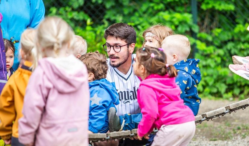 Mannlig ansatt synger sammen med barnehagebarn i bakgården