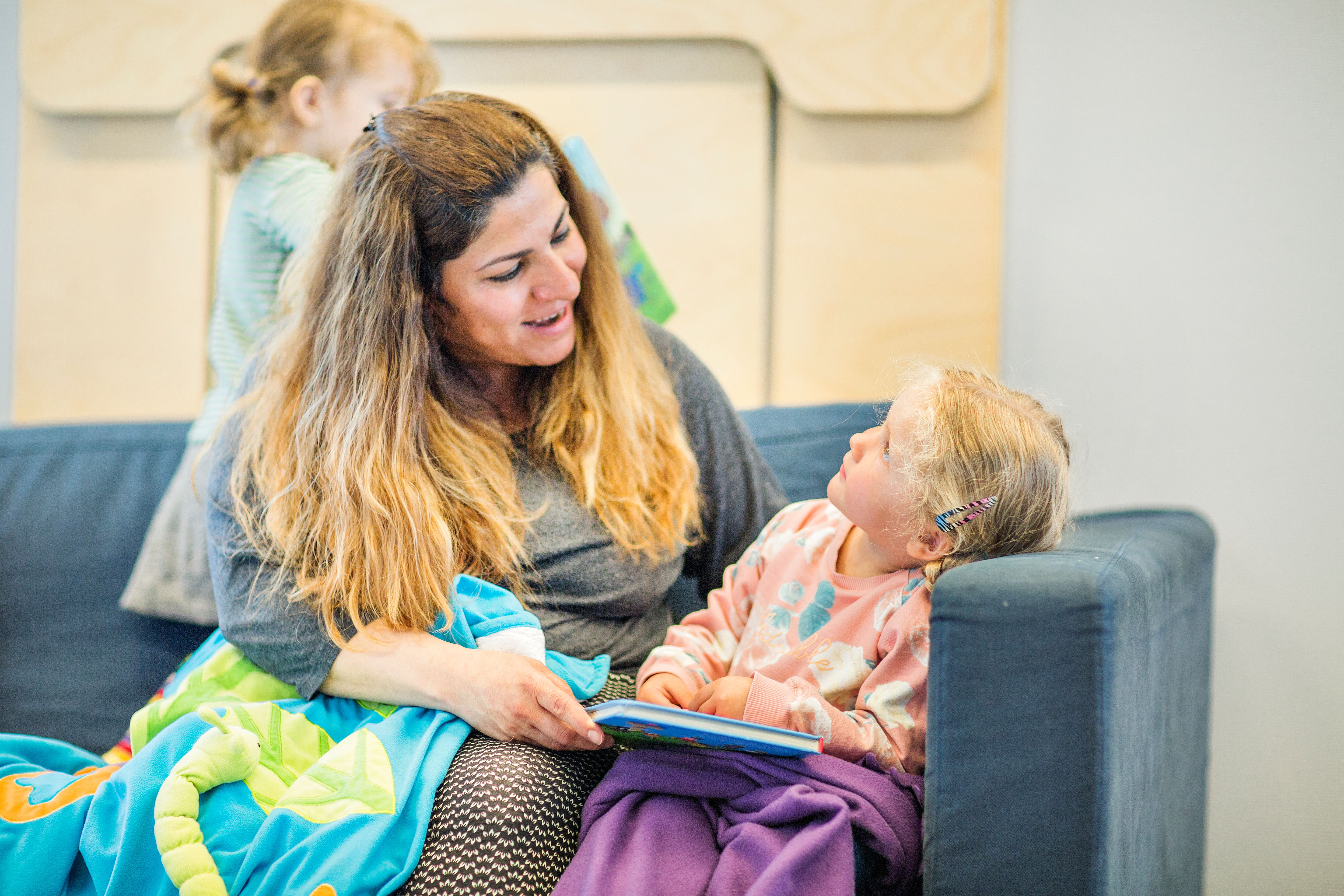 Et barn og en ansatt sitter i en sofa sammen, med en bok i fanget. Foto: Krafttak for sang