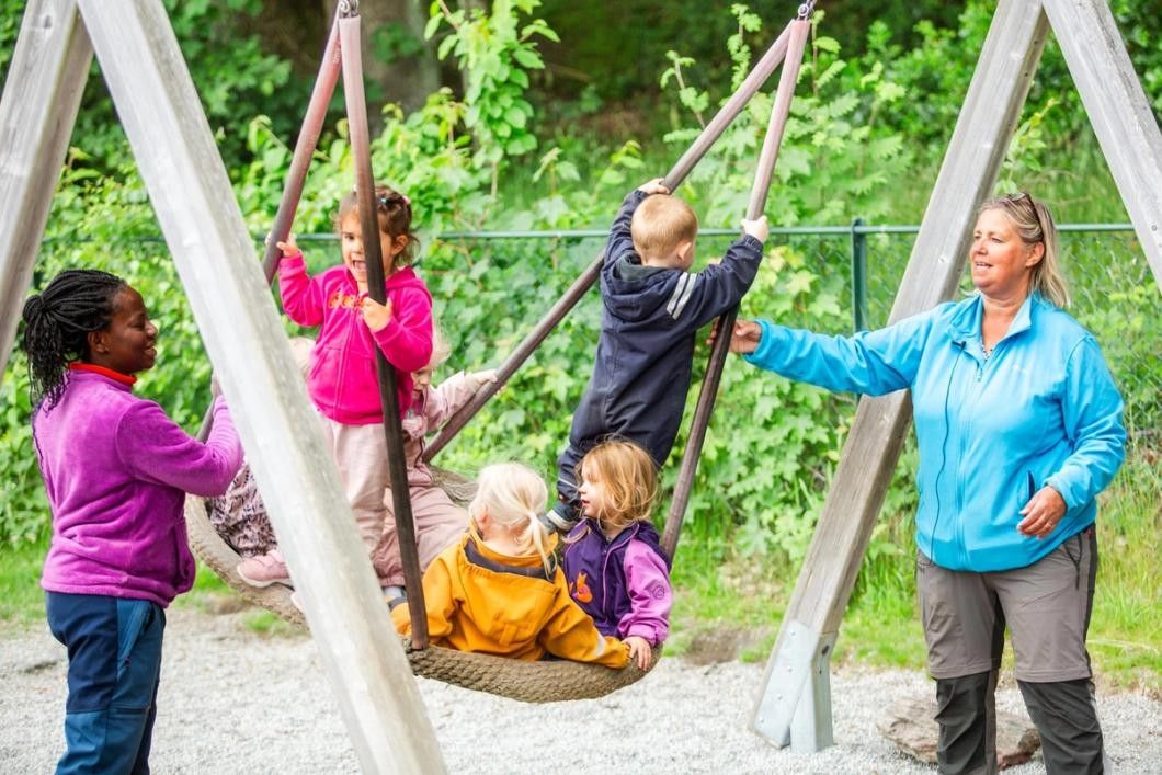 To ansatte synger og gir fart på huska, med tre barn oppi. 