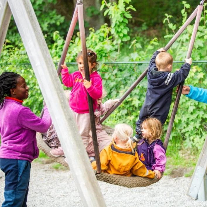 To ansatte synger og gir fart på huska, med tre barn oppi.