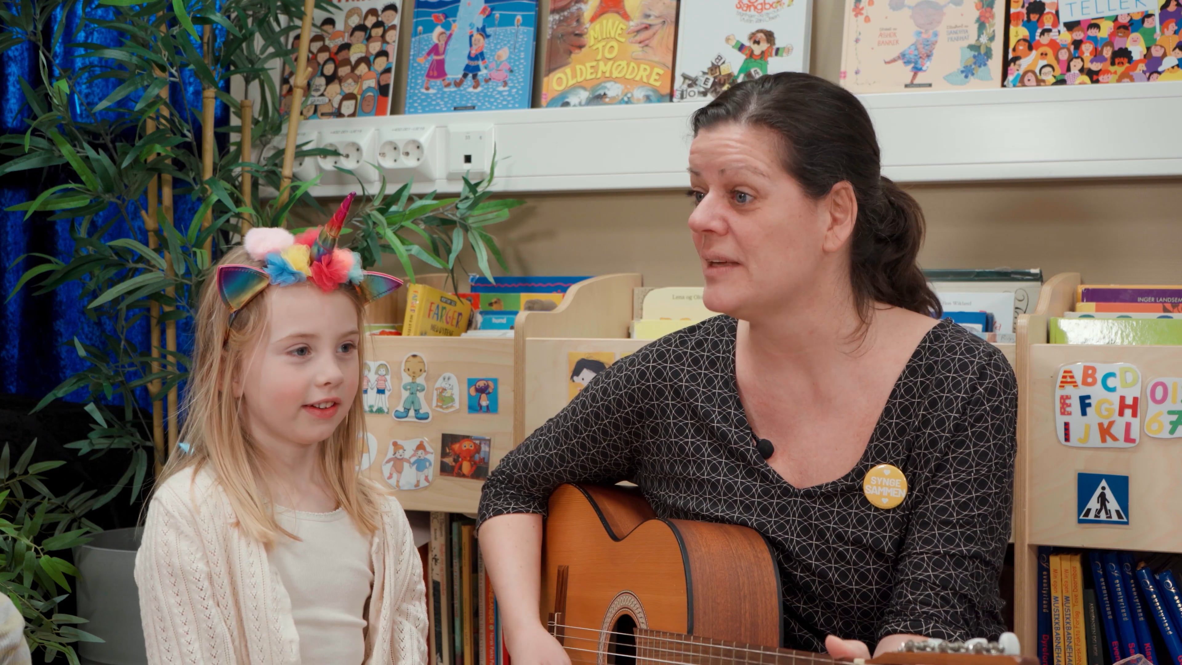 Bilde av Hanne V. Turøy som spiller gitar med et barn ved siden av seg