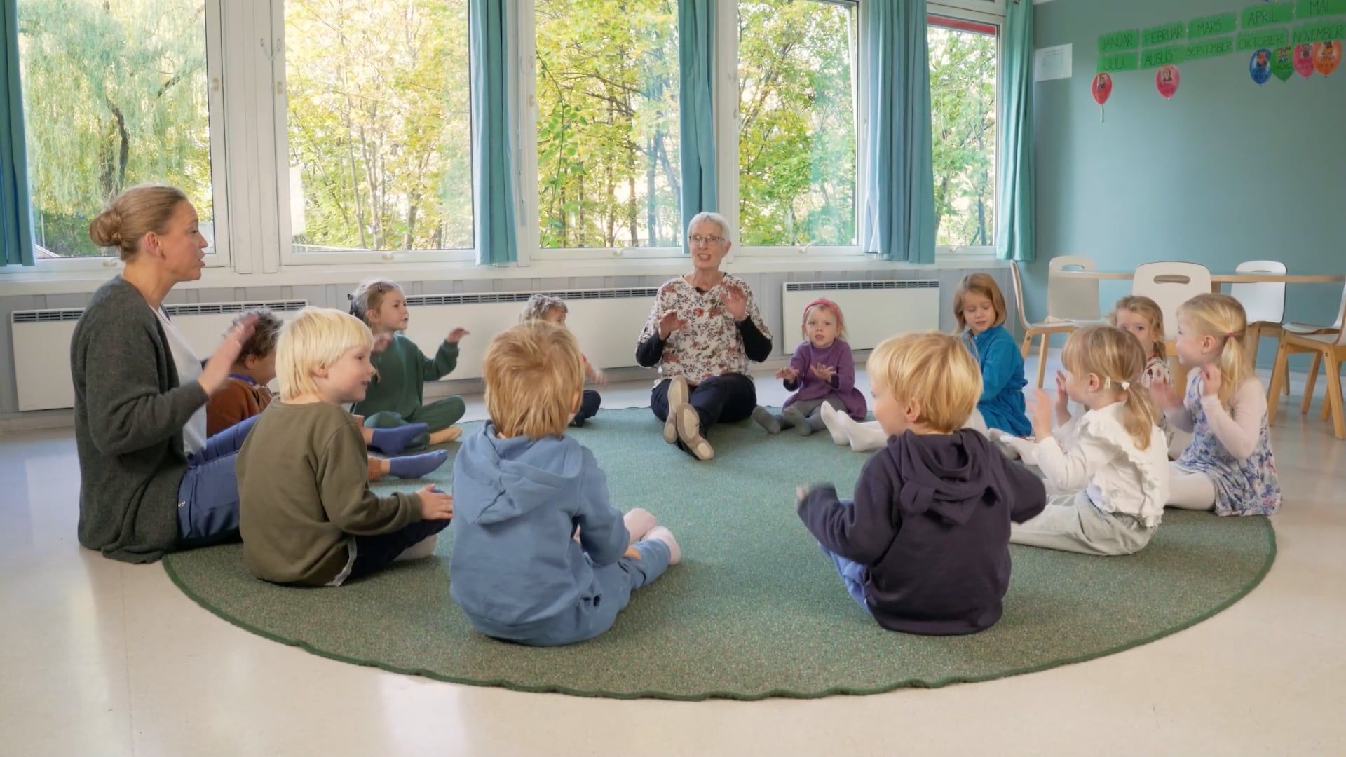 Bilde av to voksne som sitter sammen med noen barnehagebarn i samlingsstund