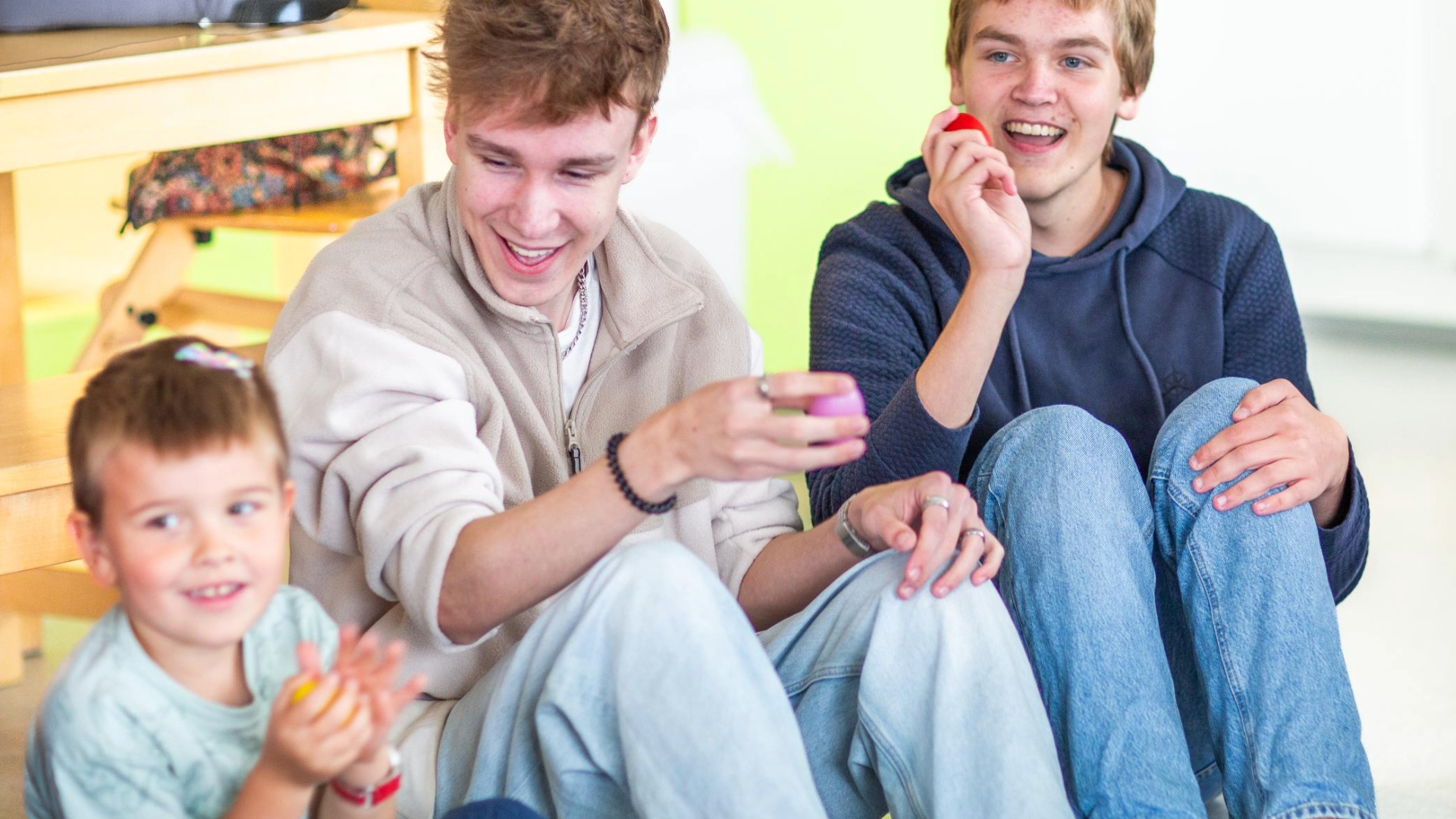 Bilde av to vgs elever som synger og spiller rasleegg med et barn